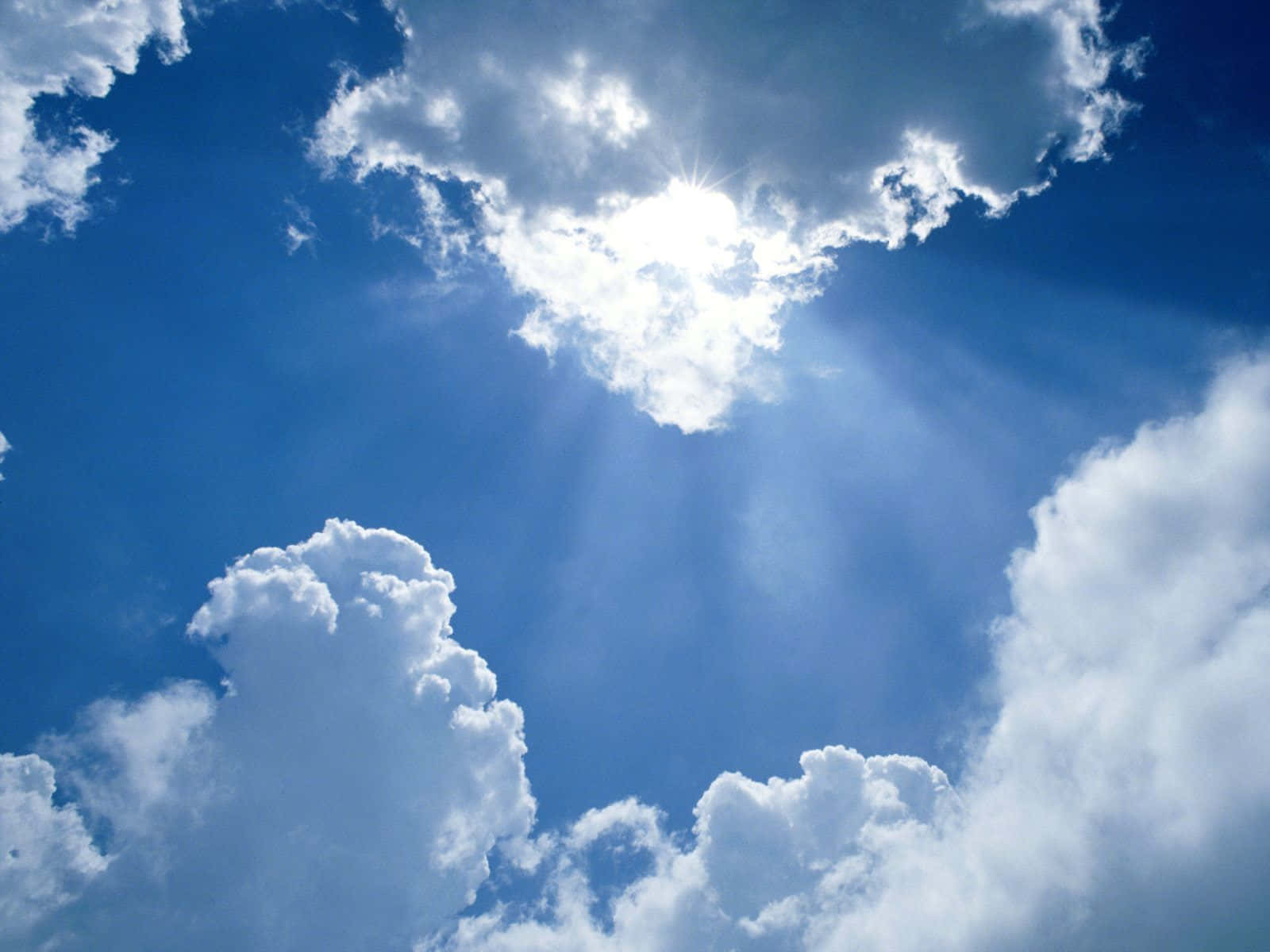 Sky Clouds 桌布 壁紙 — 陽光穿過蓬鬆的白雲，在鮮豔的藍天中輻射開來。