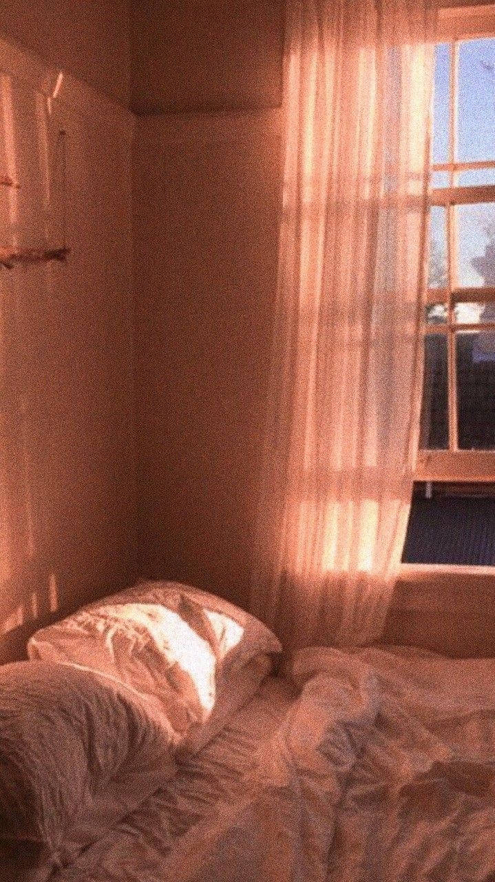 Aesthetic Bedroom 桌布 壁紙 — 陽光穿過薄紗窗簾，灑在溫暖光線下的臥室角落一張凌亂的床上。