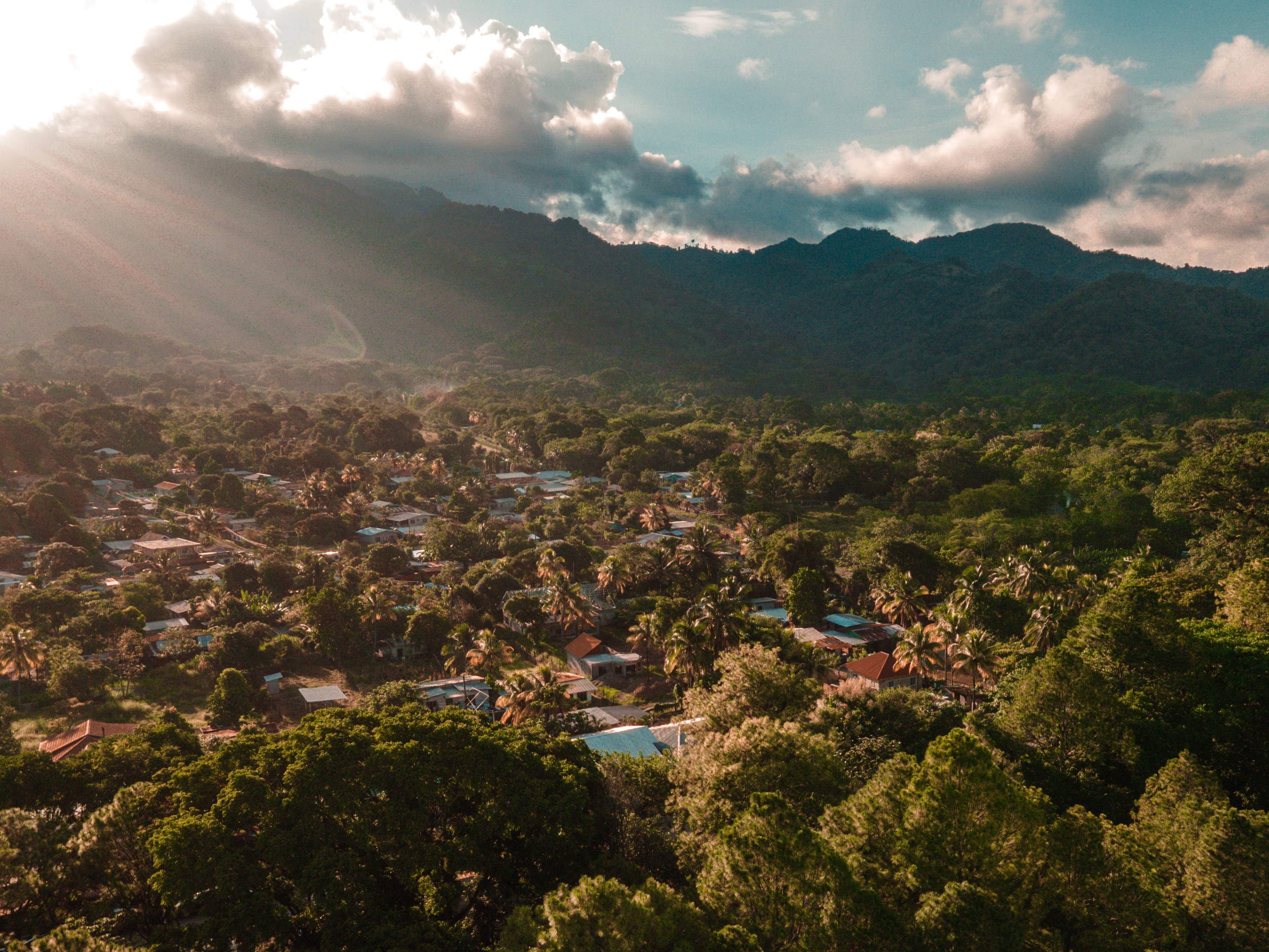 Honduras 桌布 壁紙 — 陽光穿過雲層，照亮了坐落在茂密青山中的熱帶村莊。