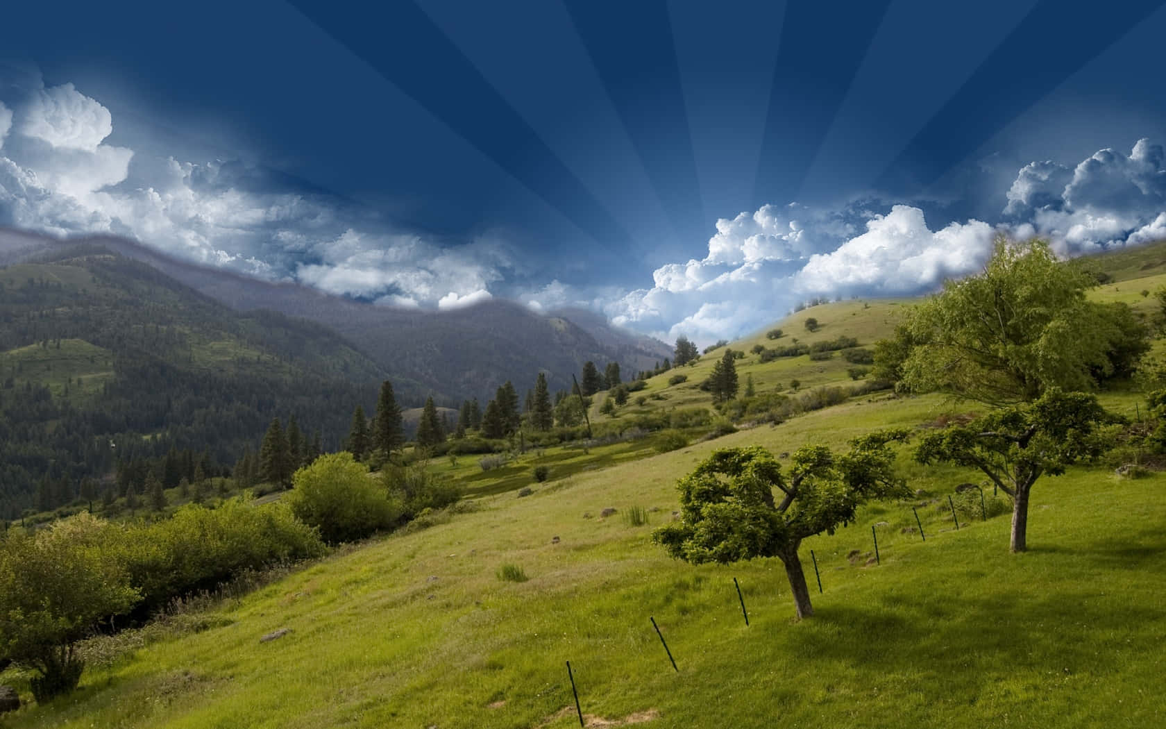風景 桌布 壁紙 — 陽光穿過雲層，照射在綠意盎然、點綴著樹木和遠山的小山上。