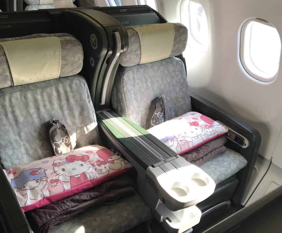 Airport 桌布 壁紙 — 陽光穿過飛機窗戶，照亮了可斜倚商務艙座位上的毛絨Hello Kitty枕頭。
