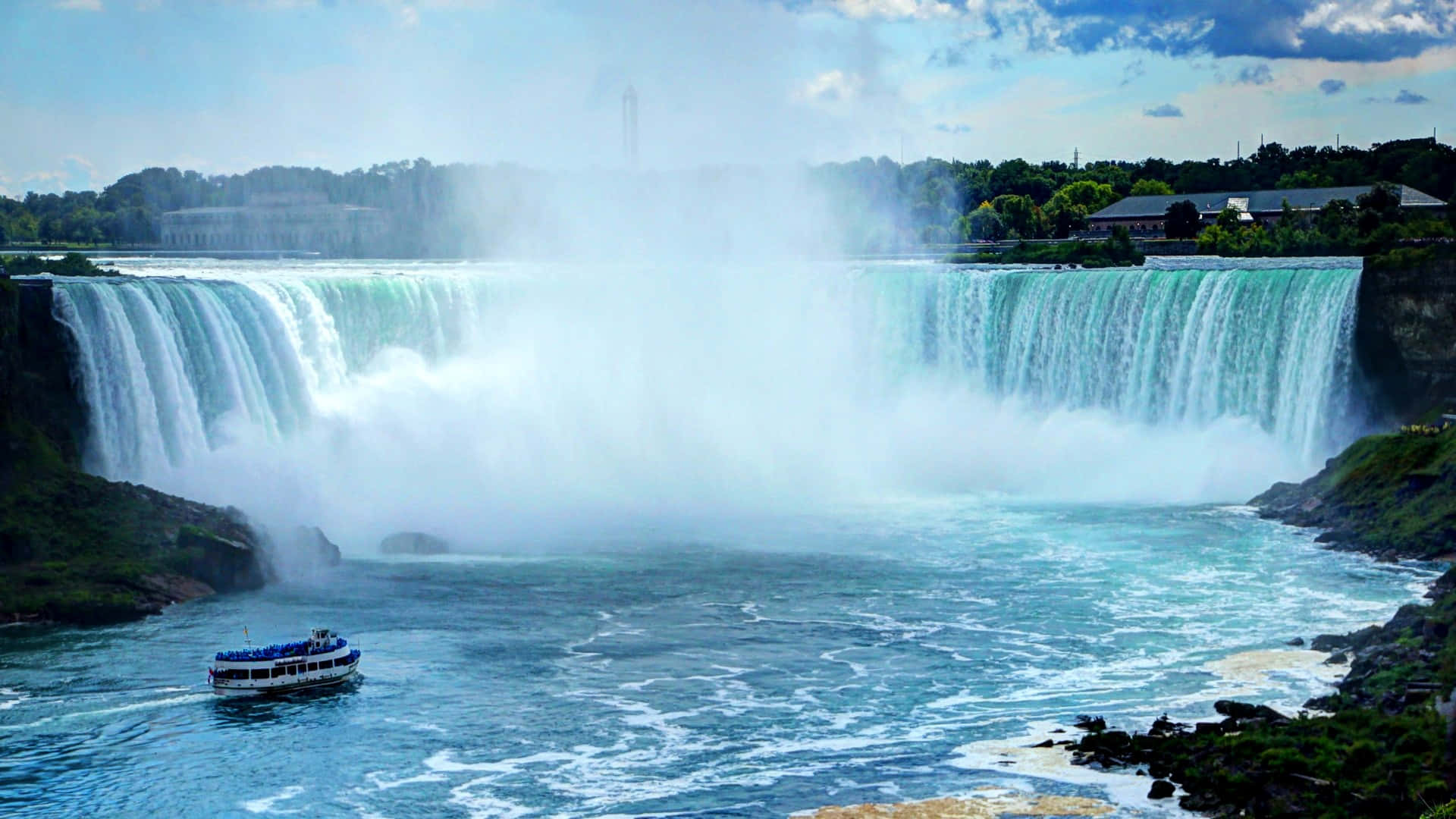 720p Niagara Falls 桌布 壁紙 — 雄偉寬闊的瀑布傾瀉而下，流入湍急的河流，一艘觀光船在下方霧氣瀰漫的水域中航行。
