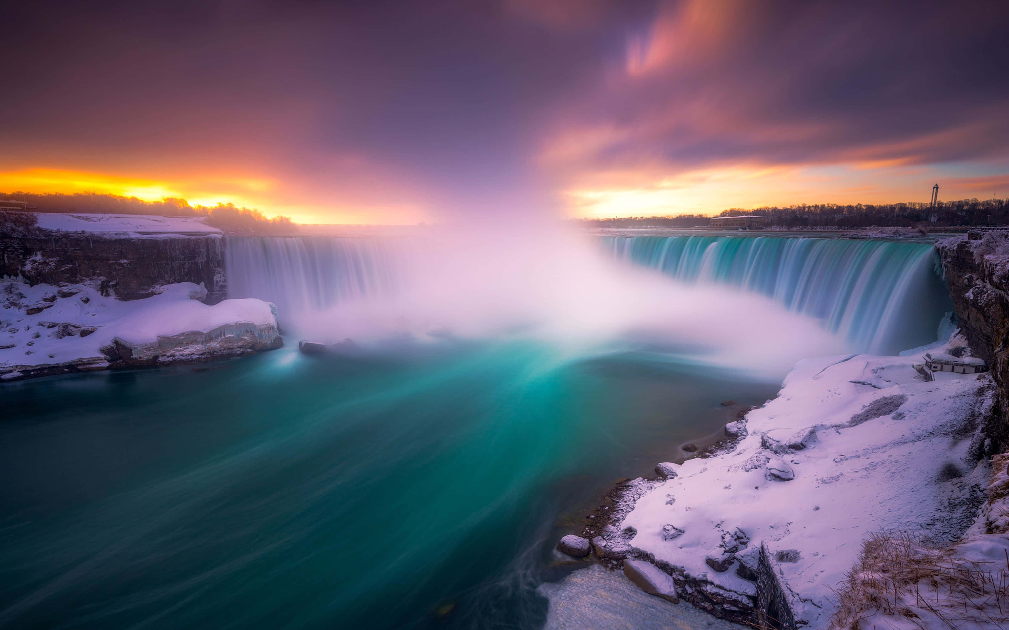 Niagara Falls 桌布 壁紙 — 雄偉的冬季瀑布在戲劇性的紫橙色日落天空下，以充滿活力的藍綠色傾瀉而下。