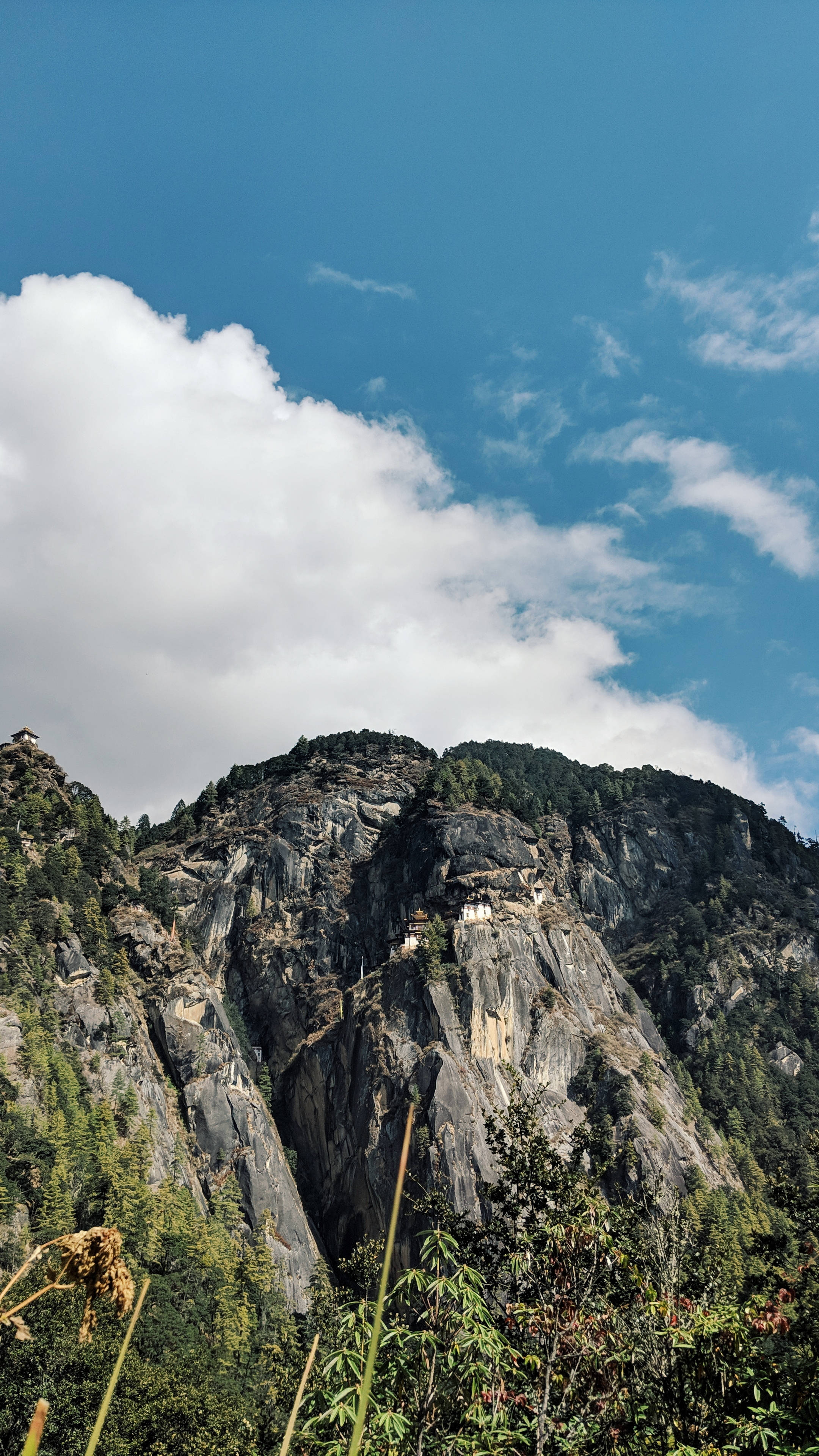 Bhutan 桌布 壁紙 — 雄偉的山峰，在明亮的藍天白雲下，一座白色小修道院緊貼在岩石面上。