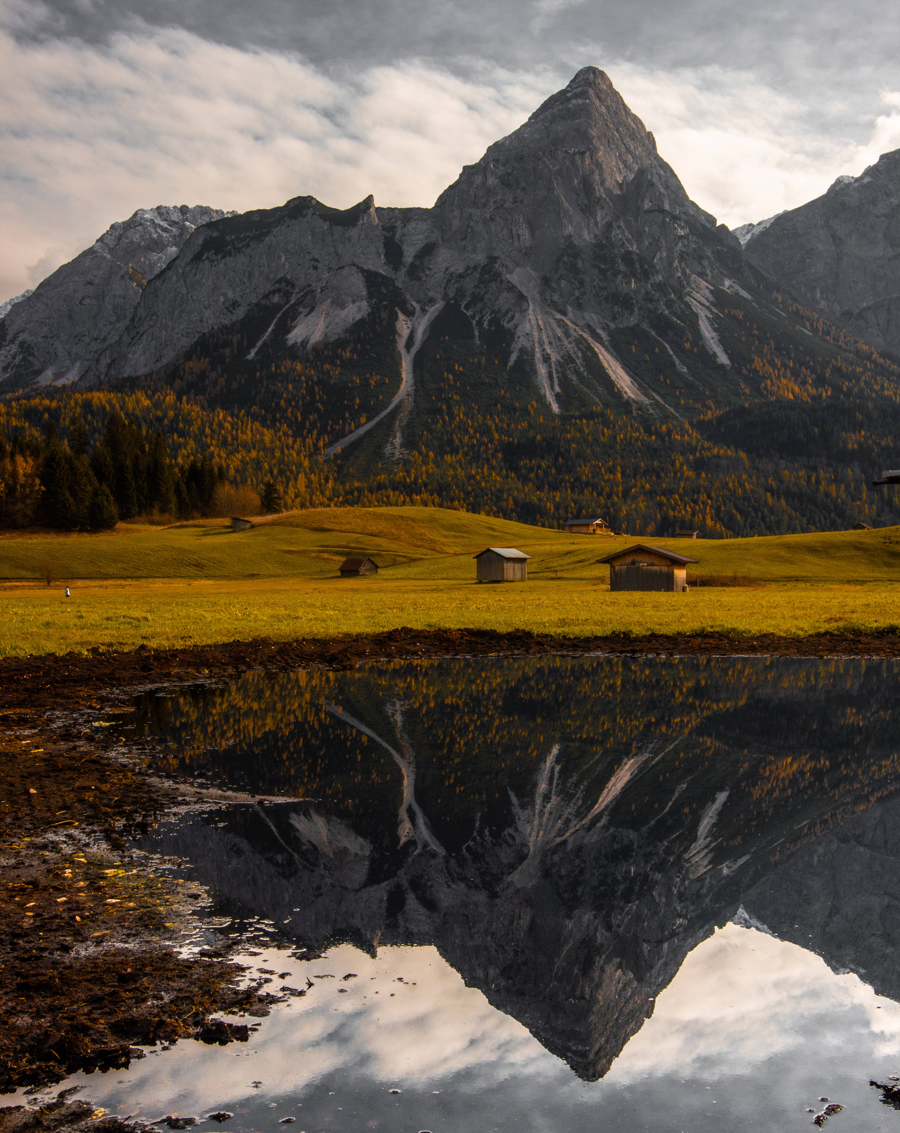 Austria 桌布 壁紙 — 雄偉的山峰完美地倒映在寧靜的高山池塘中，周圍環繞著金色的秋日草地和質樸的木屋。