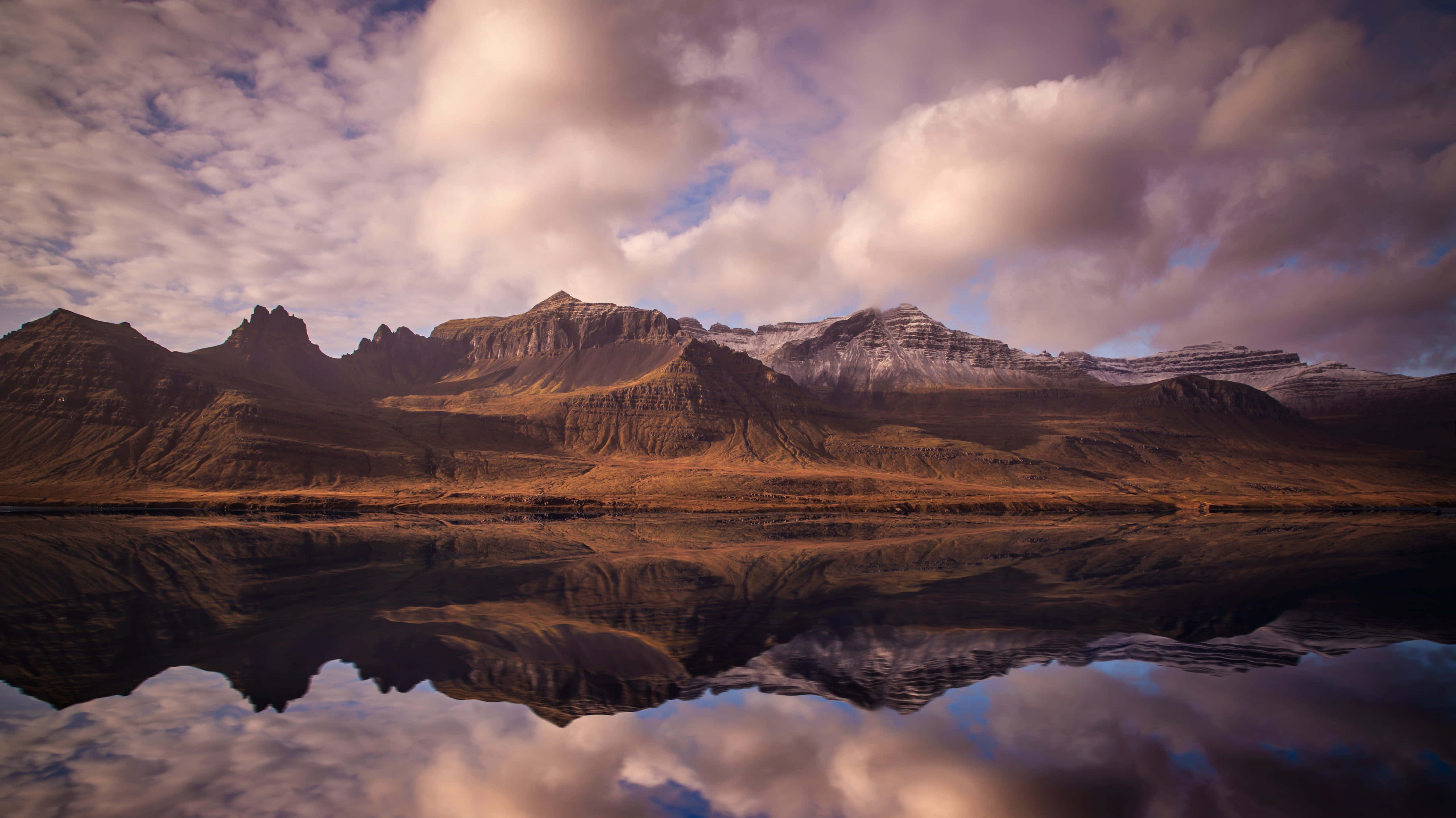 Iceland Desktop 桌布 壁紙 — 雄偉的山脈，白雪覆蓋的山峰，在戲劇性的多雲天空下，完美地倒映在平靜的湖面上。