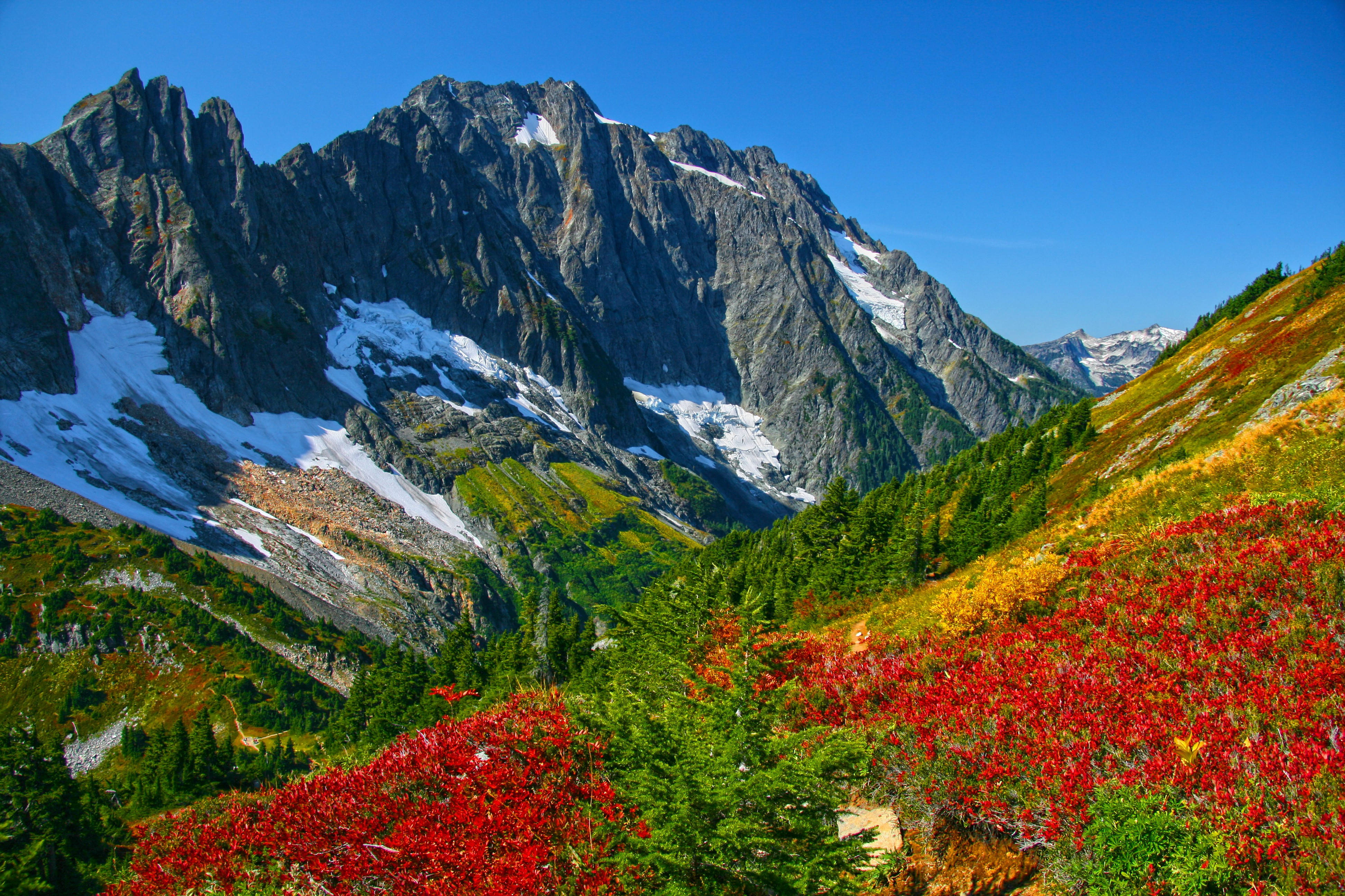 HD Mountain 桌布 壁紙 — 雄偉的山脈，白雪覆蓋的山峰，聳立在一個充滿火紅和金黃秋葉的山谷之上，天空清澈湛藍。