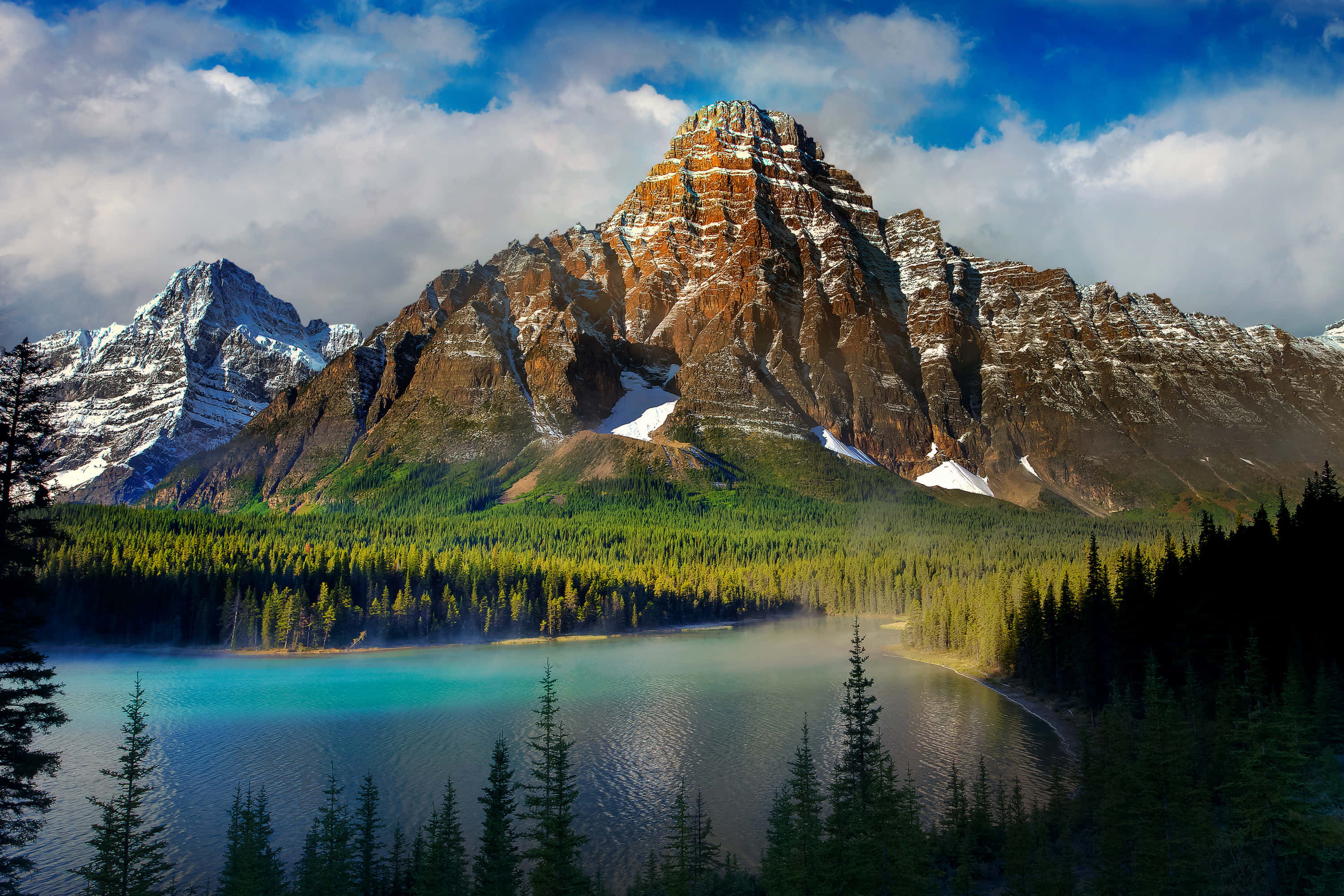 Mountain Landscape 桌布 壁紙 — 雄偉的山脈，白雪覆蓋的山峰聳立在寧靜的碧綠湖泊之上，周圍是茂密的常綠森林，天空多雲。