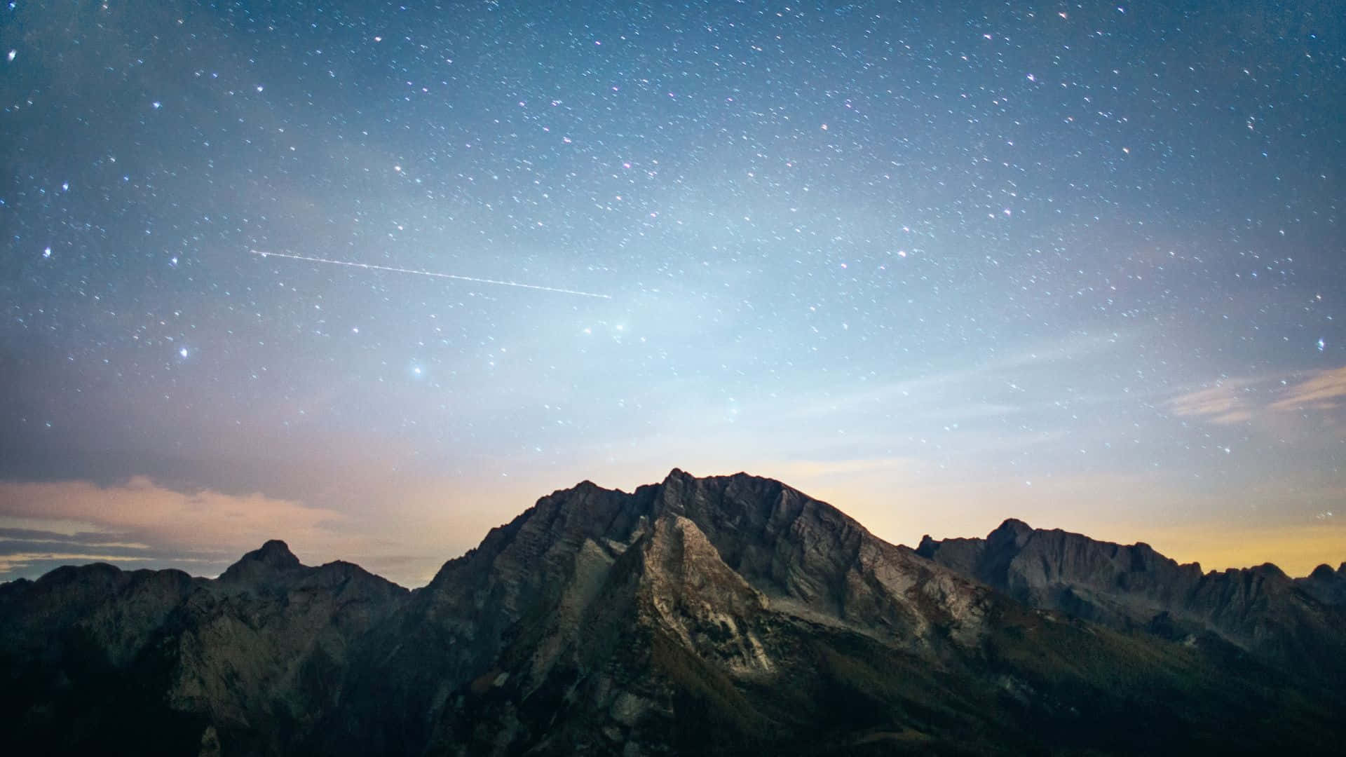 星空動畫 桌布 壁紙 — 雄偉的山脈在繁星點點的暮色天空中呈現剪影，一顆明亮的流星劃過天際。