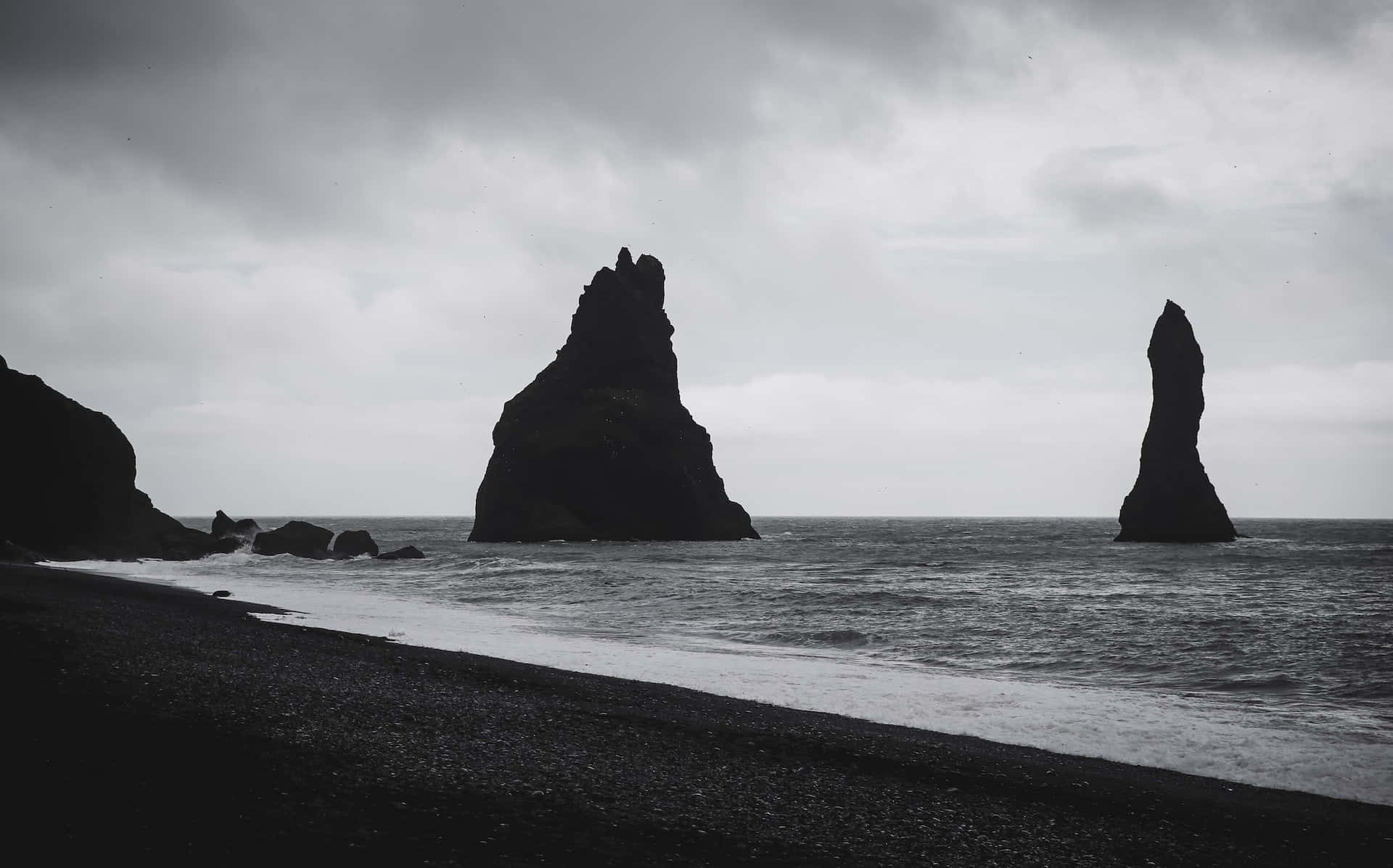 Black And White Beach 桌布 壁紙 — 雄偉的海蝕柱從黑色的火山沙灘上聳立，天空陰沉密佈。