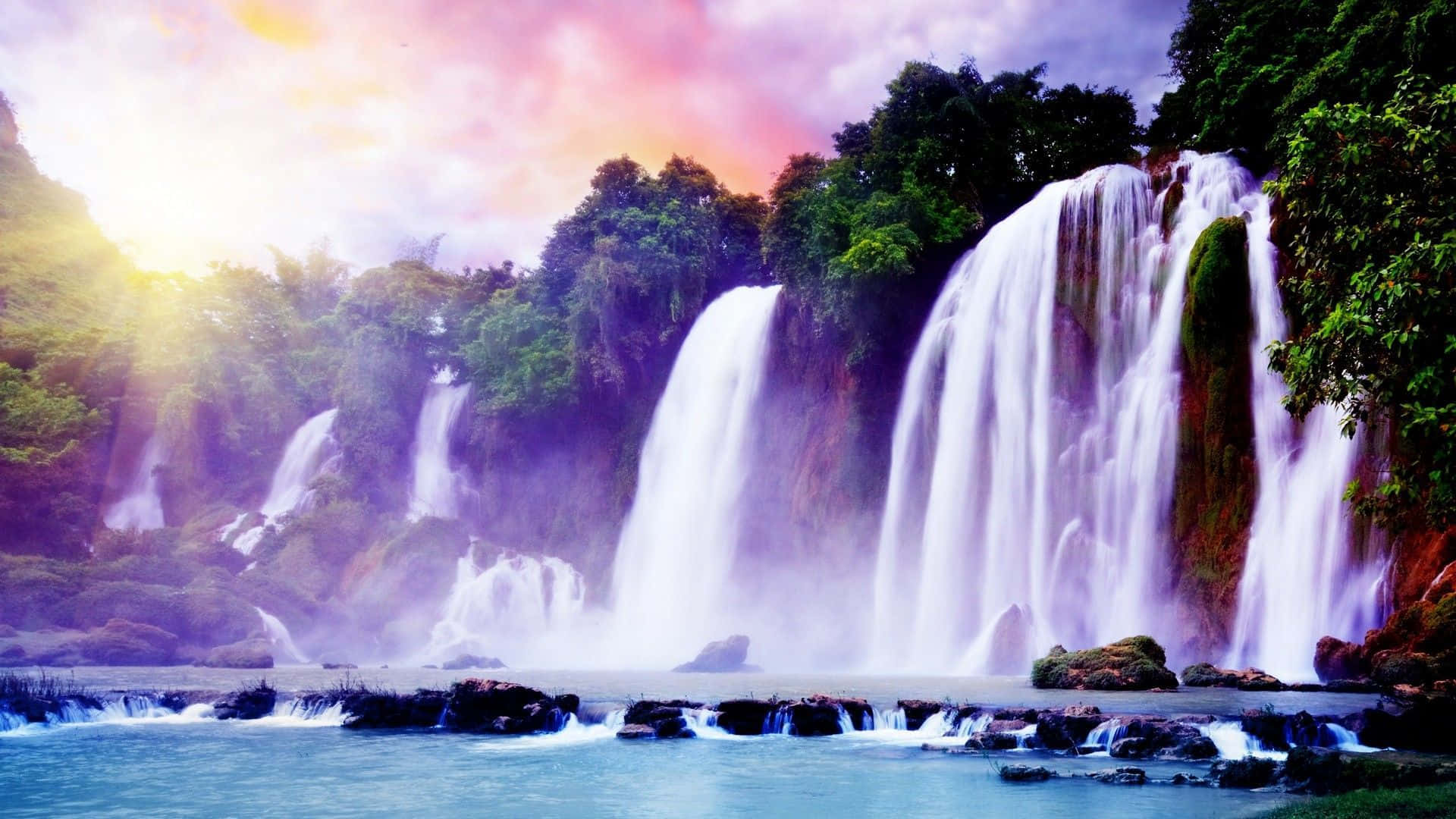 Waterfalls 桌布 壁紙 — 雄偉的瀑布在生機勃勃的日出天空下，穿過茂密的綠色叢林傾瀉而下。
