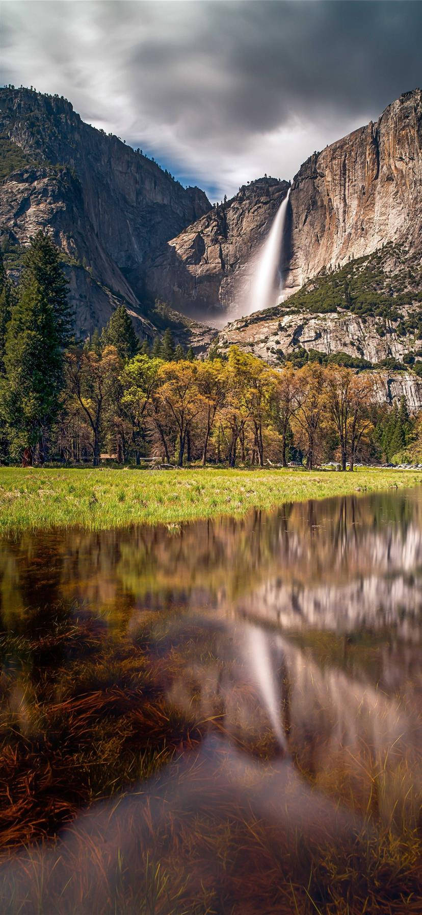 Yosemite iPhone 桌布 壁紙 — 雄偉的瀑布從花崗岩懸崖傾瀉而下，流入平靜的池塘，倒映著秋樹和暴風雨的天空。