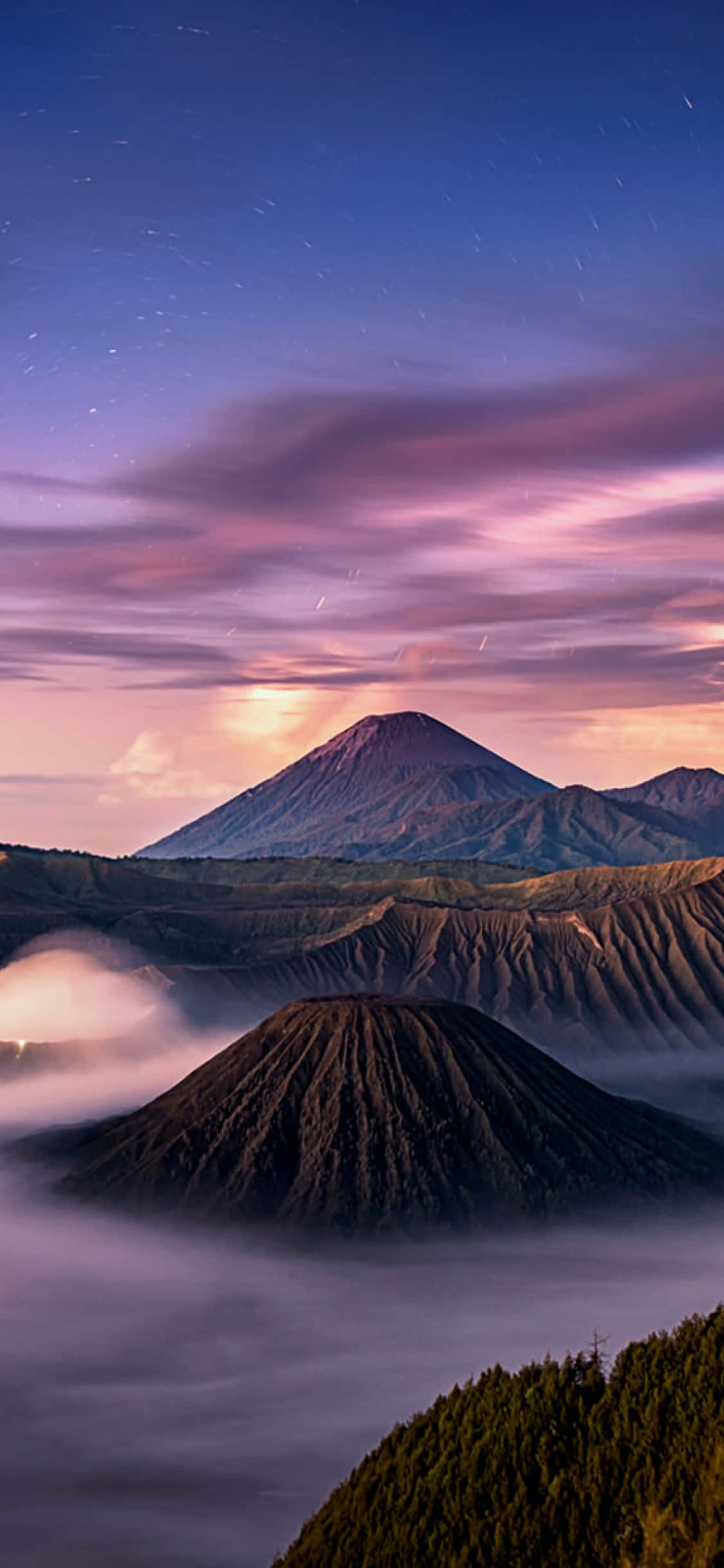 Calming iPhone 桌布 壁紙 — 雄偉的火山山脈從雲海中升起，在星空暮色天空下呈現粉紅和紫色調。