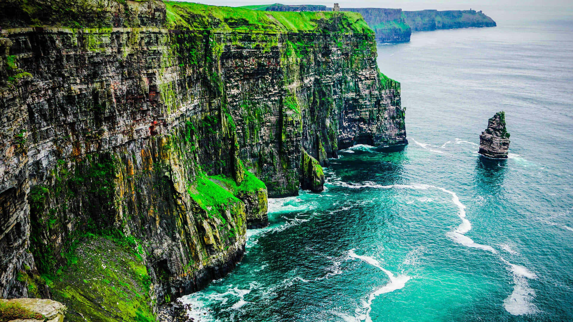 Ireland Desktop 桌布 壁紙 — 雄偉的綠色懸崖直插碧綠海水，海浪在陰天下拍打岩石突出部分。