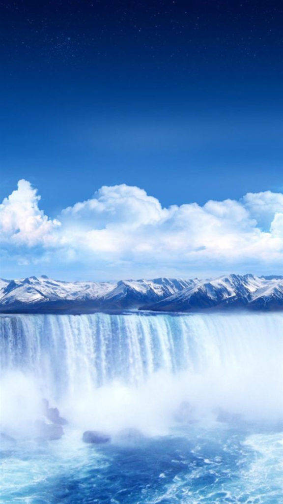 自然 桌布 壁紙 — 雄偉的雪山山脈俯瞰著在蔚藍天空和蓬鬆白雲下奔騰而下的瀑布。