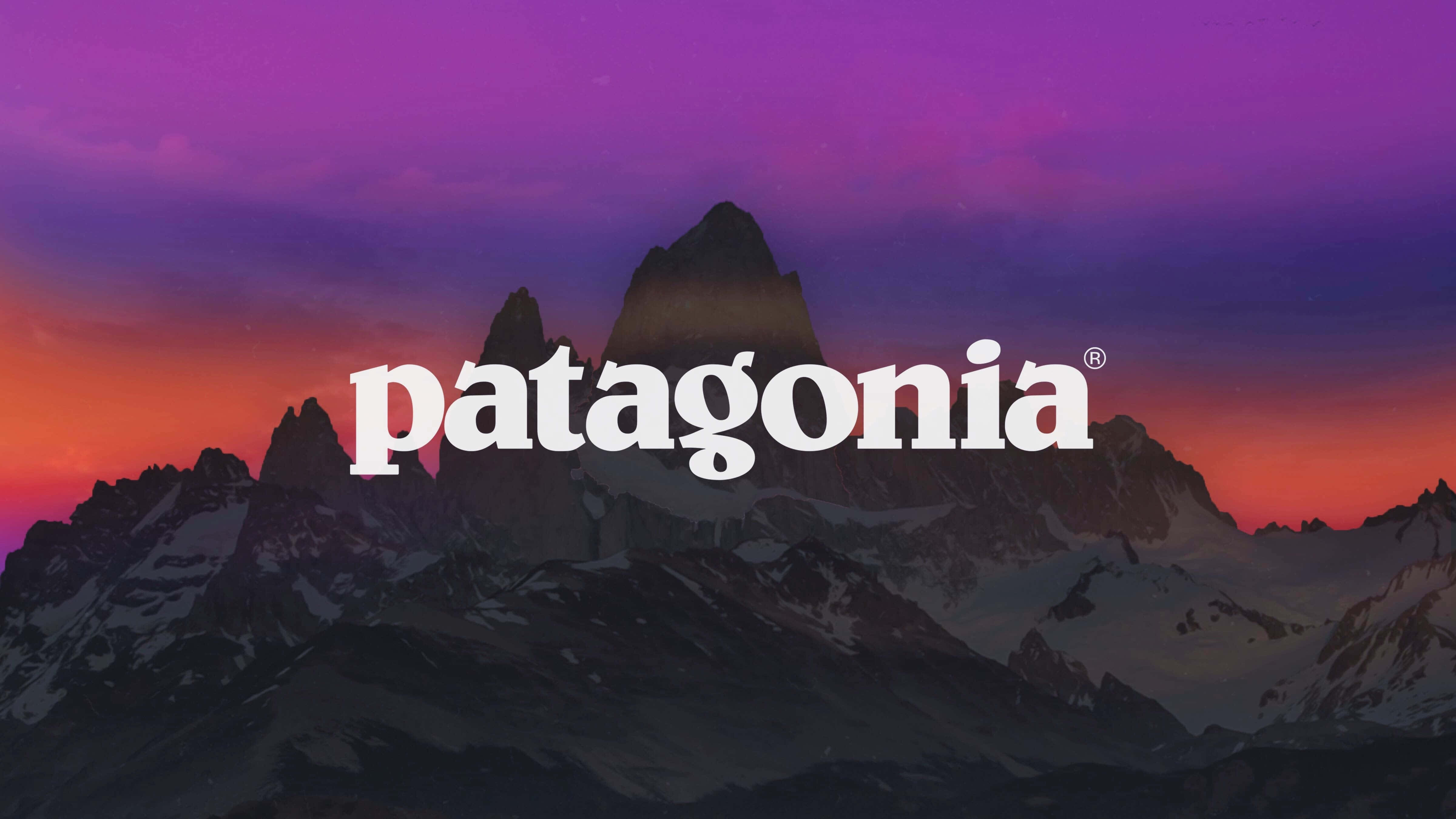 Patagonia 桌布 壁紙 — 雄偉的雪山山脈在充滿活力的紫色和橙色日落天空的襯托下呈現出剪影，Patagonia 標誌醒目地展示。