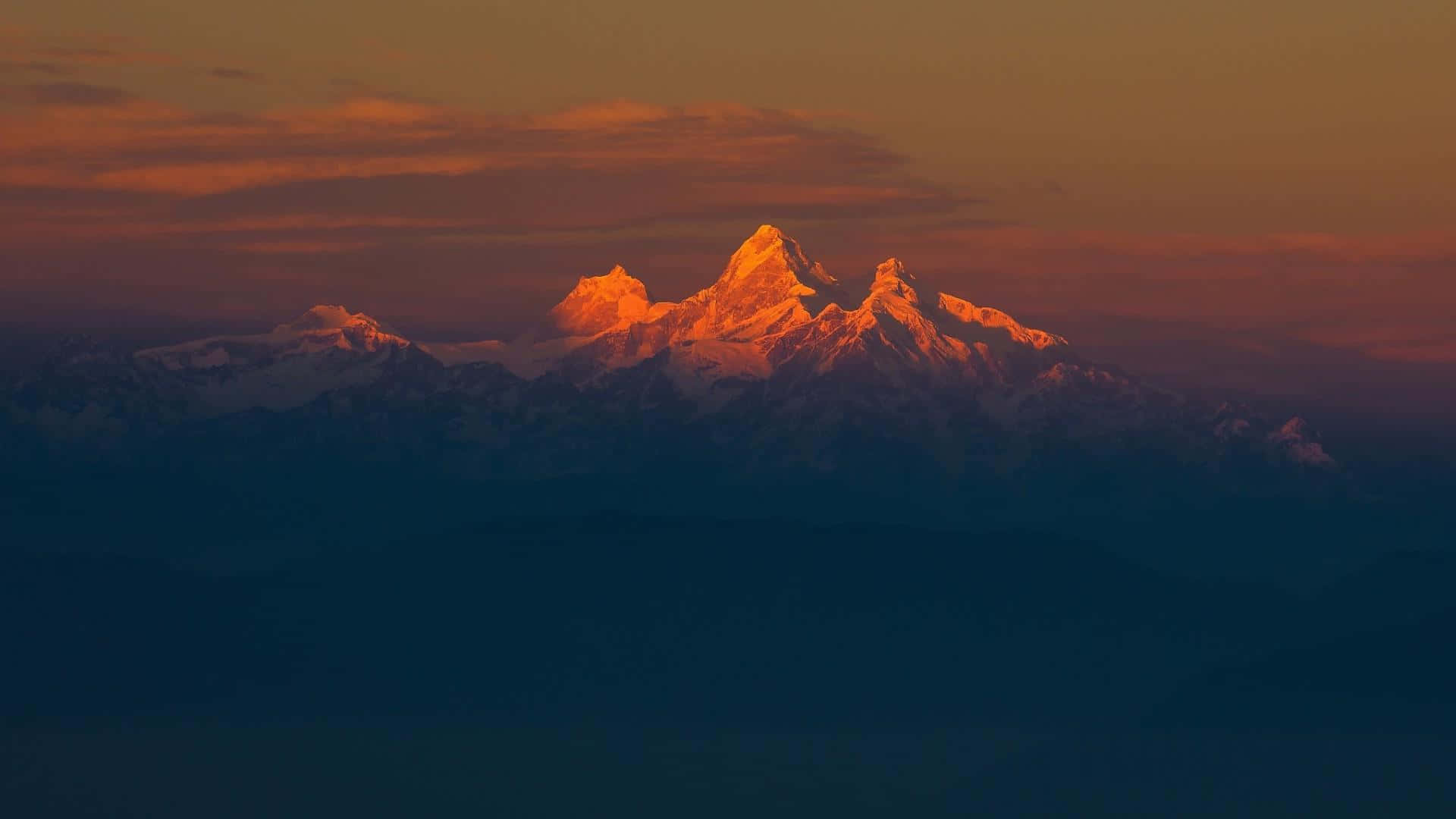 Minimalist Sunset 桌布 壁紙 — 雄偉的雪山山脈在日落時分，在漸變的天空映襯下，散發出火橙色的光芒。