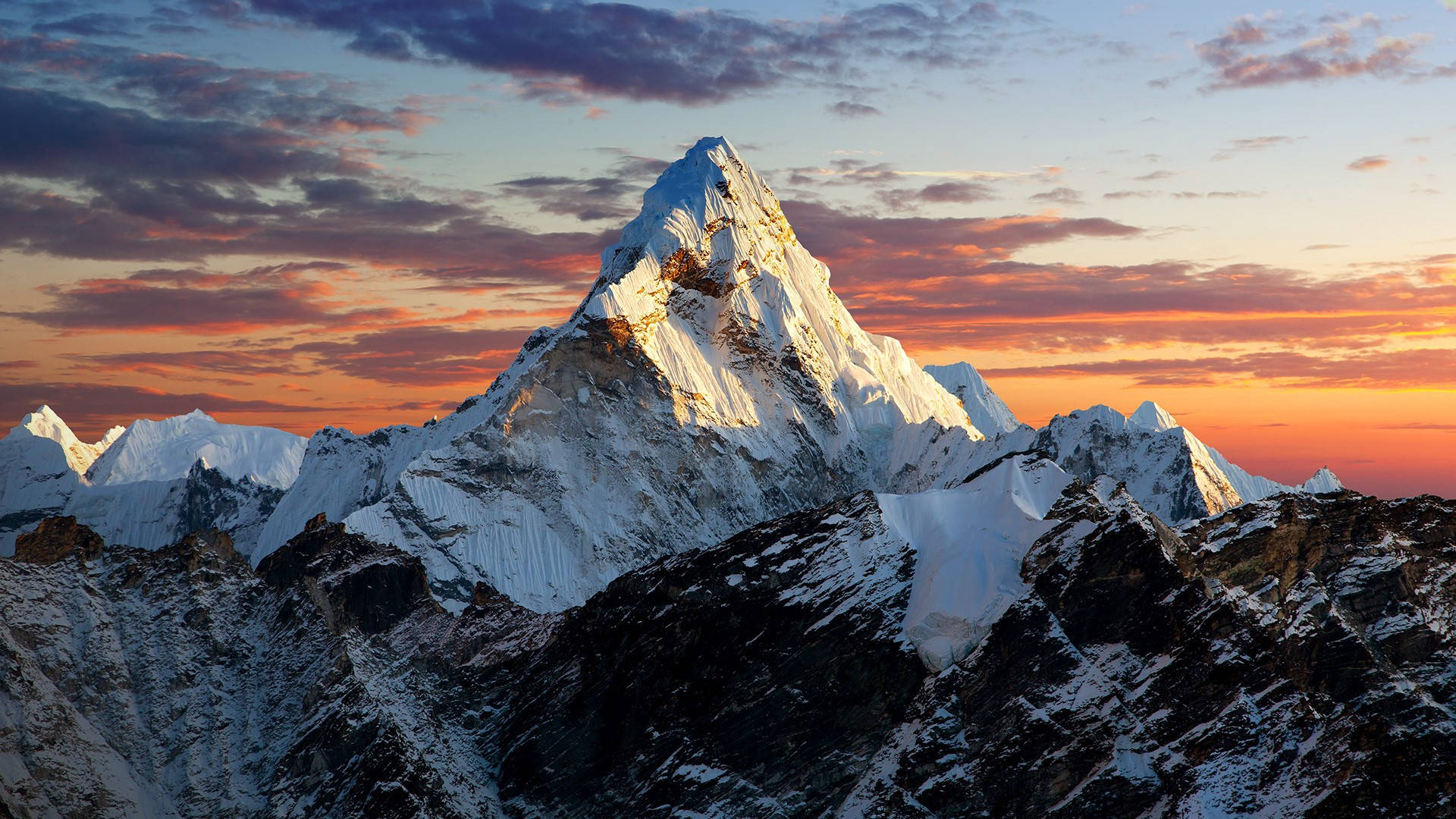 Nepal 桌布 壁紙 — 雄偉的雪山峰在日落時分閃耀著金色光芒，映襯著火紅橙紫的天空。