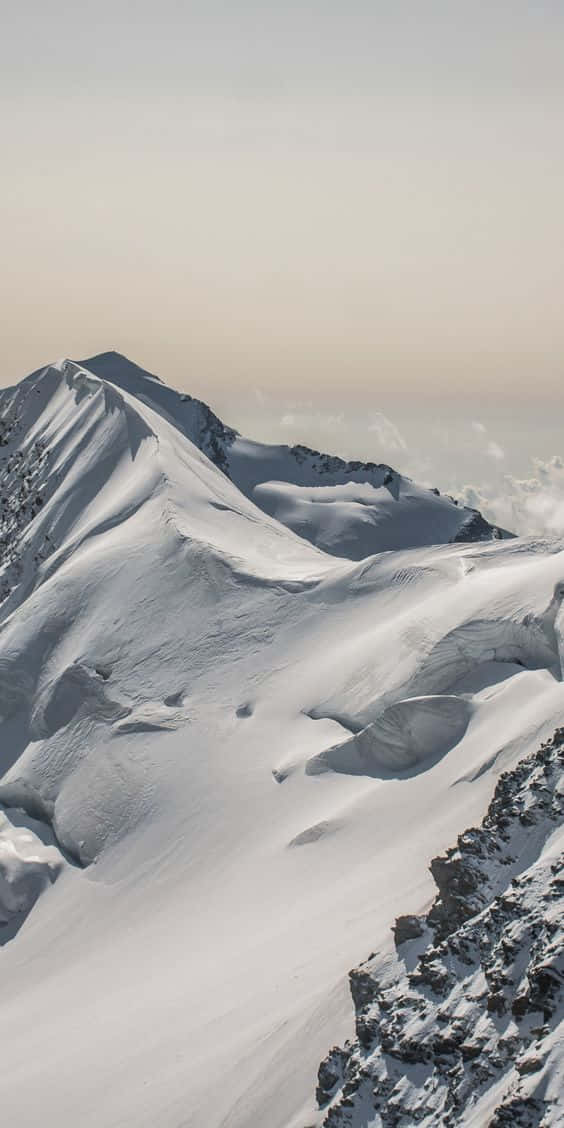 Snow iPhone 桌布 壁紙 — 雄偉的雪山峰頂在柔和粉彩的天空和下方縷縷雲彩中尖銳聳立。