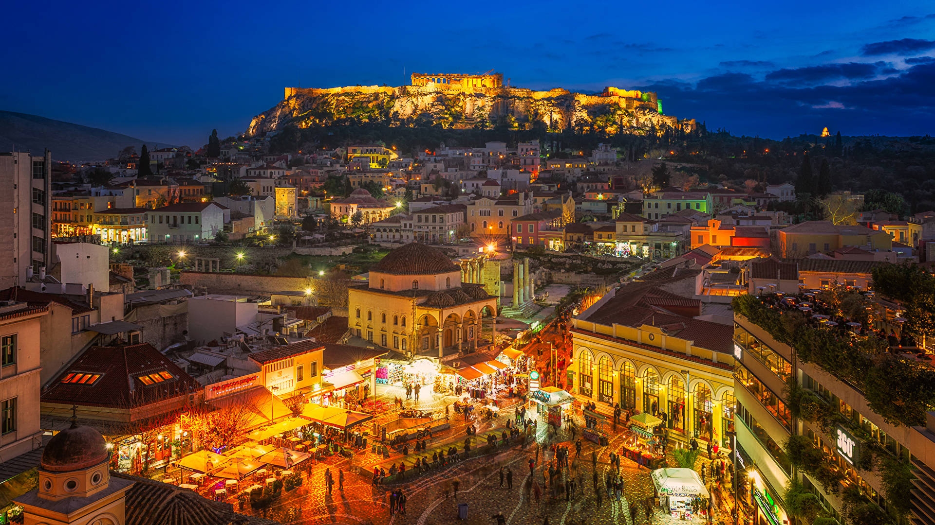 Athens 桌布 壁紙 — 雅典充滿活力的黃昏景色，衛城在山頂上閃耀，俯瞰著充滿溫暖燈光和人群的繁華城市景觀。