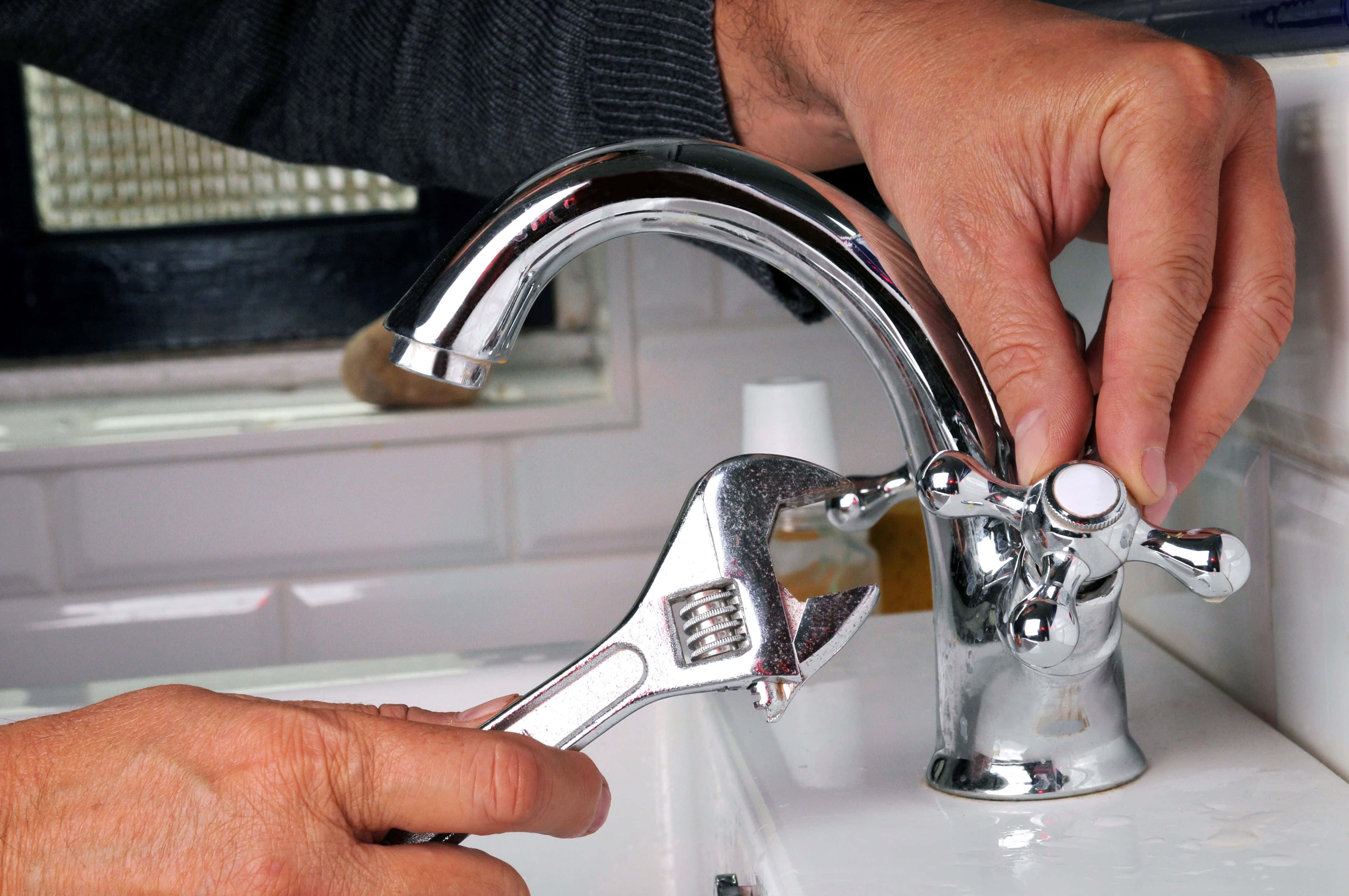 Plumbing 桌布 壁紙 — 雙手使用扳手修理白色洗手台上閃亮鍍鉻水龍頭的近距離特寫。