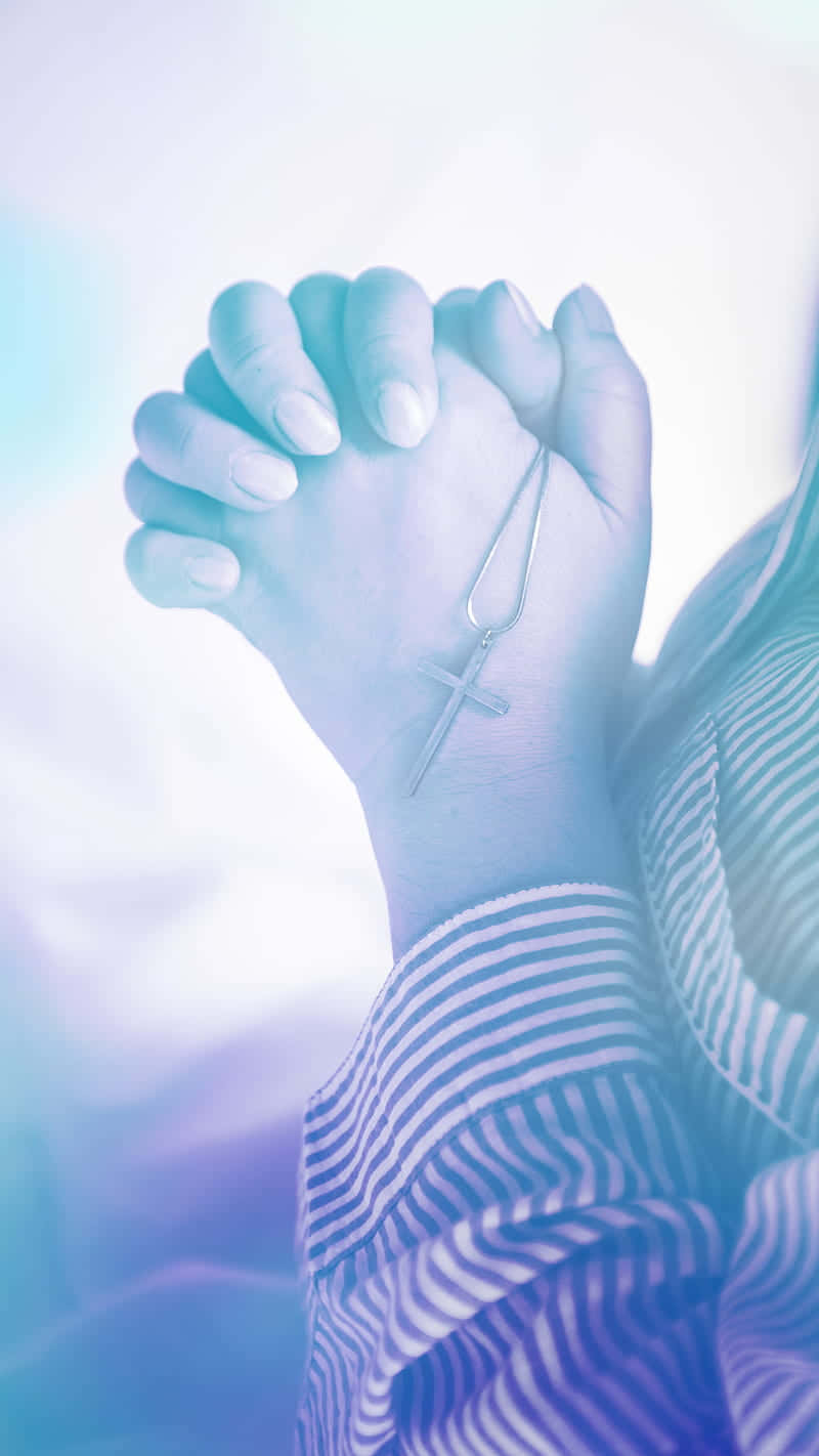 Praying 桌布 壁紙 — 雙手合十祈禱，戴著十字架項鍊，背景是柔和的藍色和紫色發光。