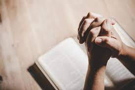 Praying 桌布 壁紙 — 雙手合十祈禱，擱在木質表面上的一本打開的書本上，沐浴在溫暖的光線中。
