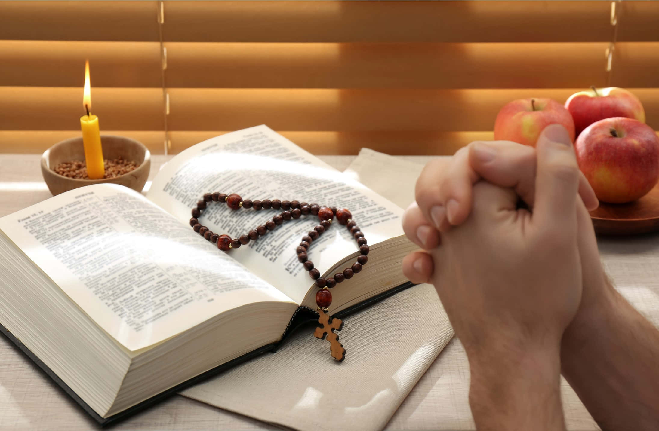 Lent 桌布 壁紙 — 雙手合十祈禱，放在打開的聖經上，旁邊有玫瑰念珠、點燃的蠟燭和紅蘋果，置於木桌上。