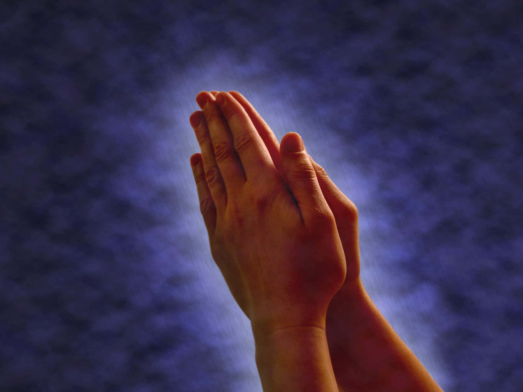 Praying 桌布 壁紙 — 雙手合十祈禱，背景為深藍色紋理，帶有柔和發光的光線。