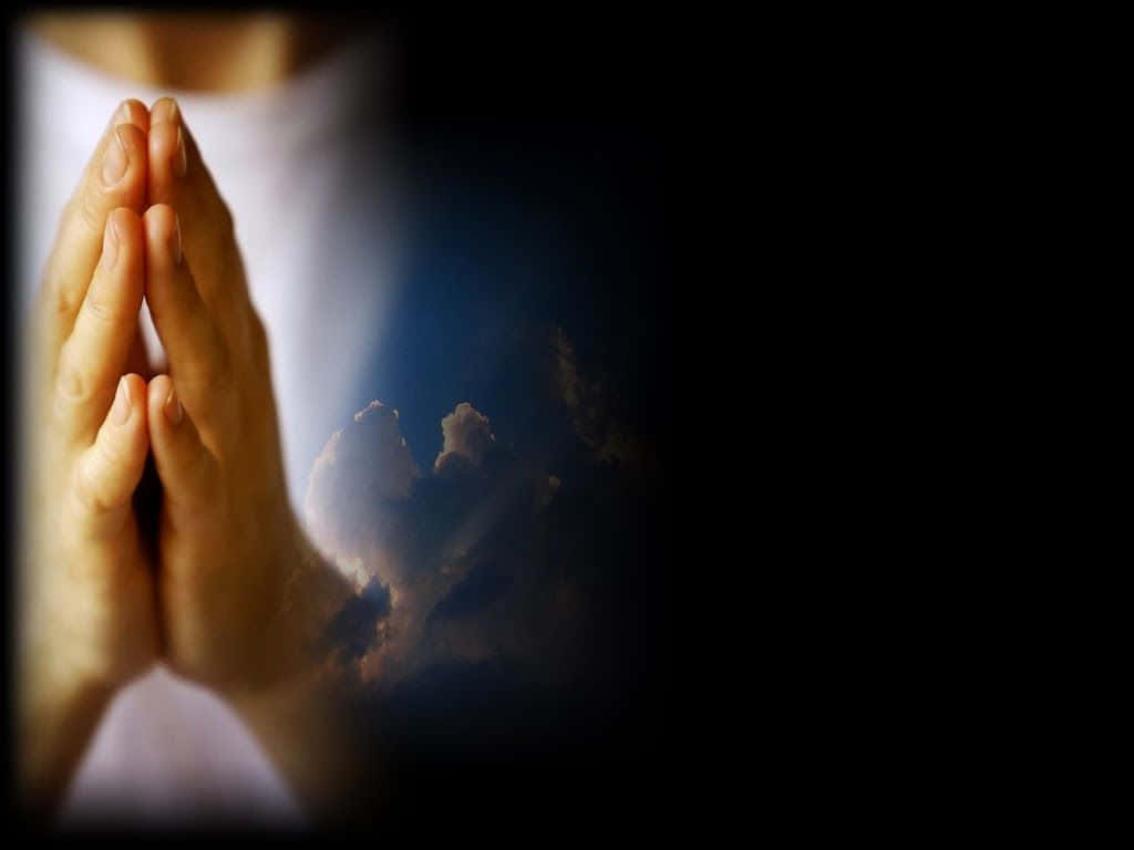 Praying 桌布 壁紙 — 雙手合十祈禱的特寫，背景是黑暗且帶有柔和發光的雲層。