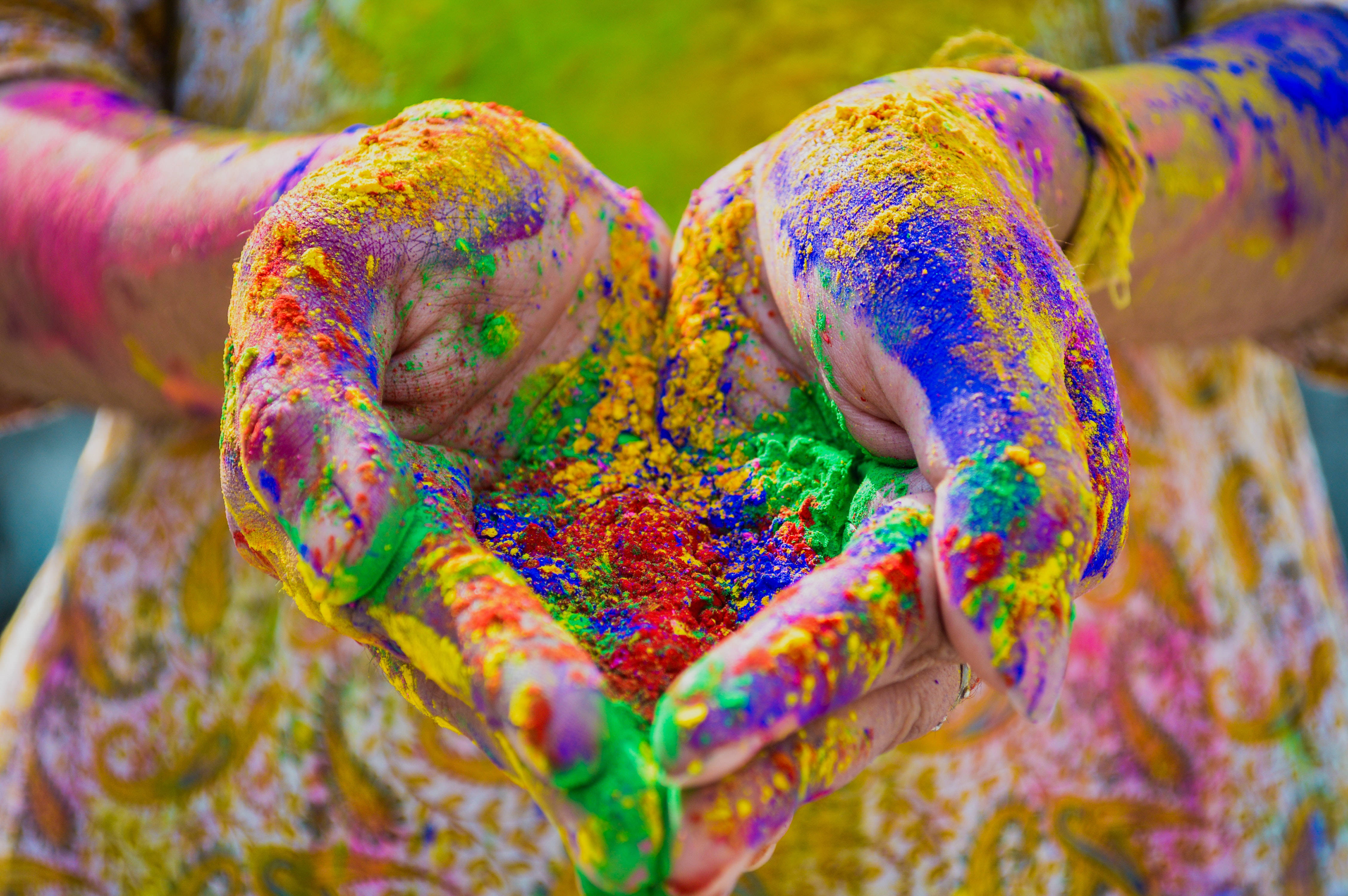 Holi 桌布 壁紙 — 雙手合攏捧著鮮豔彩色粉末的特寫，皮膚和衣服濺滿節日色彩。