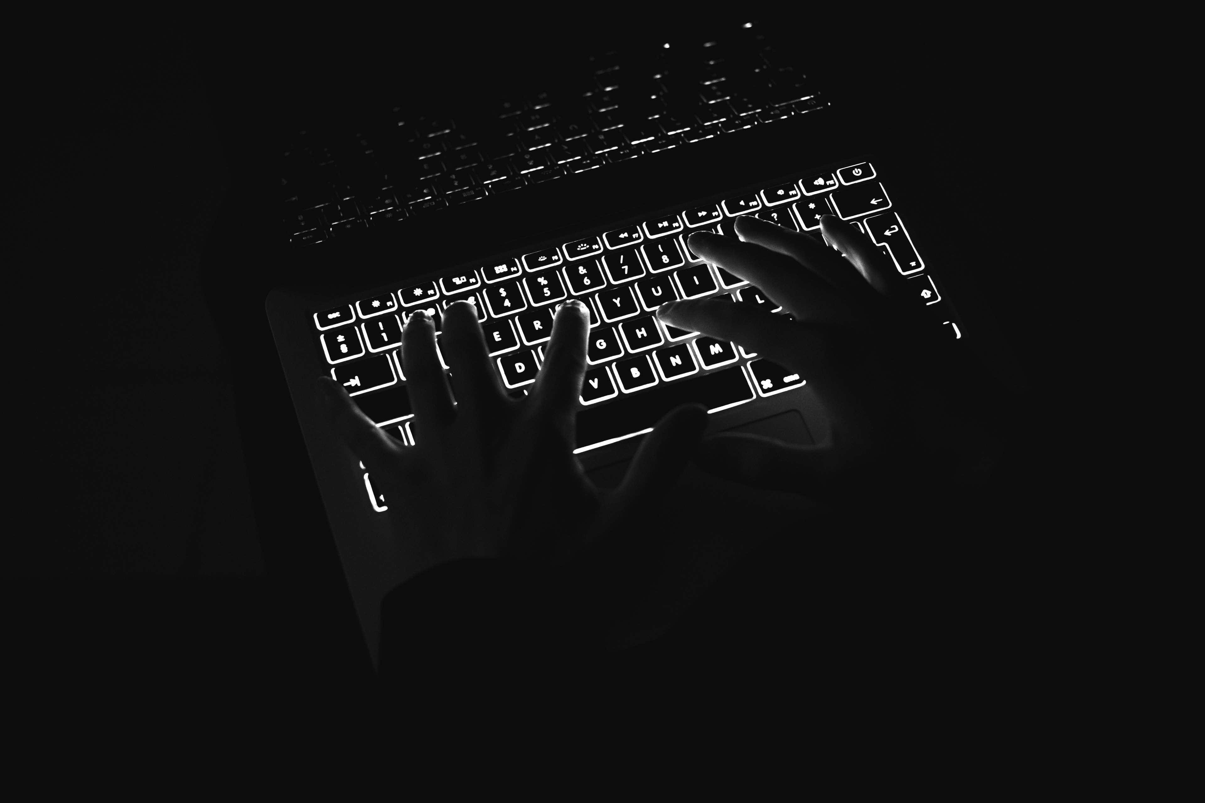 Minimalist Technology 桌布 壁紙 — 雙手在完全黑暗的環境中於發光的筆記型電腦鍵盤上打字，形成鮮明的高對比剪影。