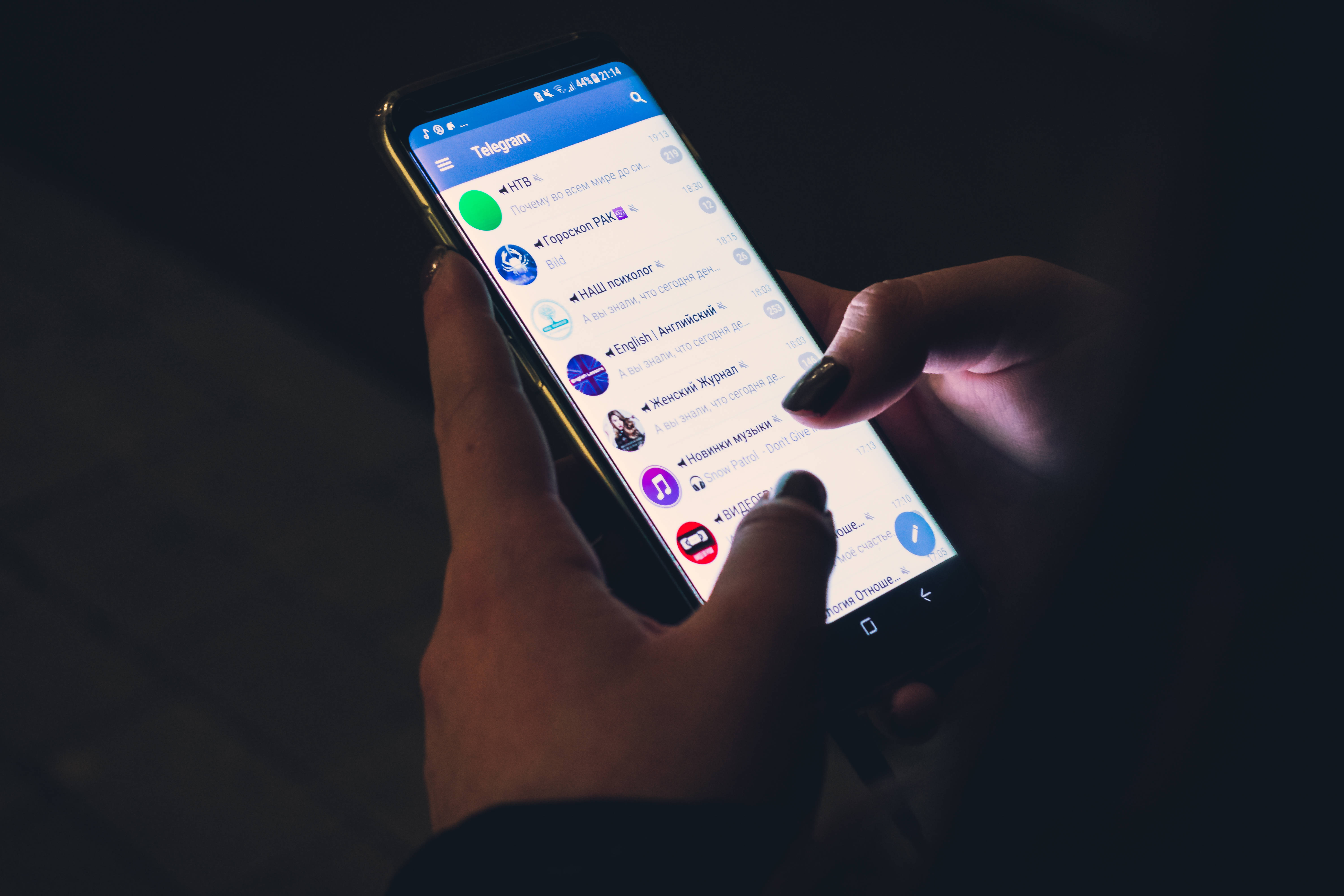 Telegram 桌布 壁紙 — 雙手在昏暗環境中拿著亮起Telegram應用程式的智慧型手機。