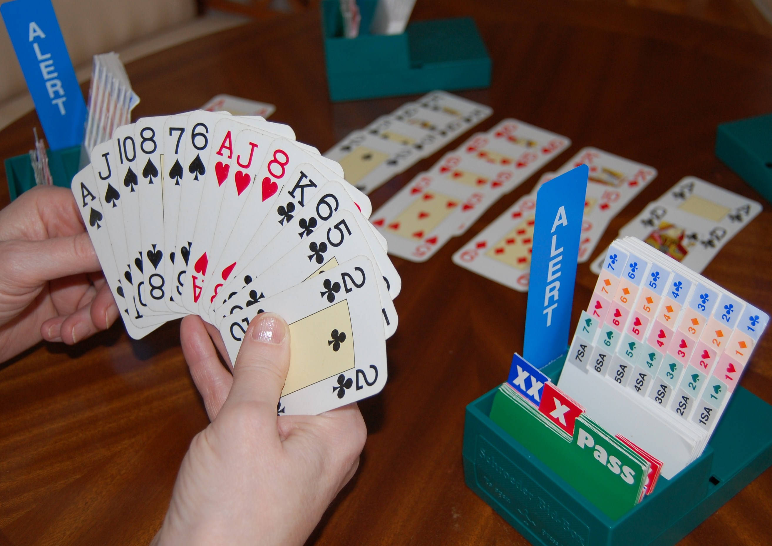 game 桌布 壁紙 — 雙手在木桌上扇開一副撲克牌，配有綠色卡牌遊戲配件和散落的卡牌。