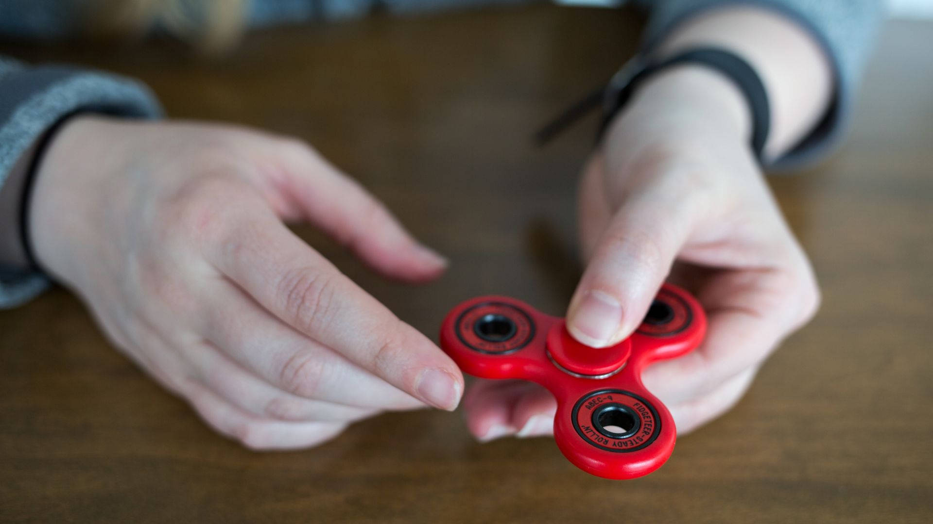 toys 桌布 壁紙 — 雙手在木桌上旋轉亮紅色指尖陀螺的特寫。