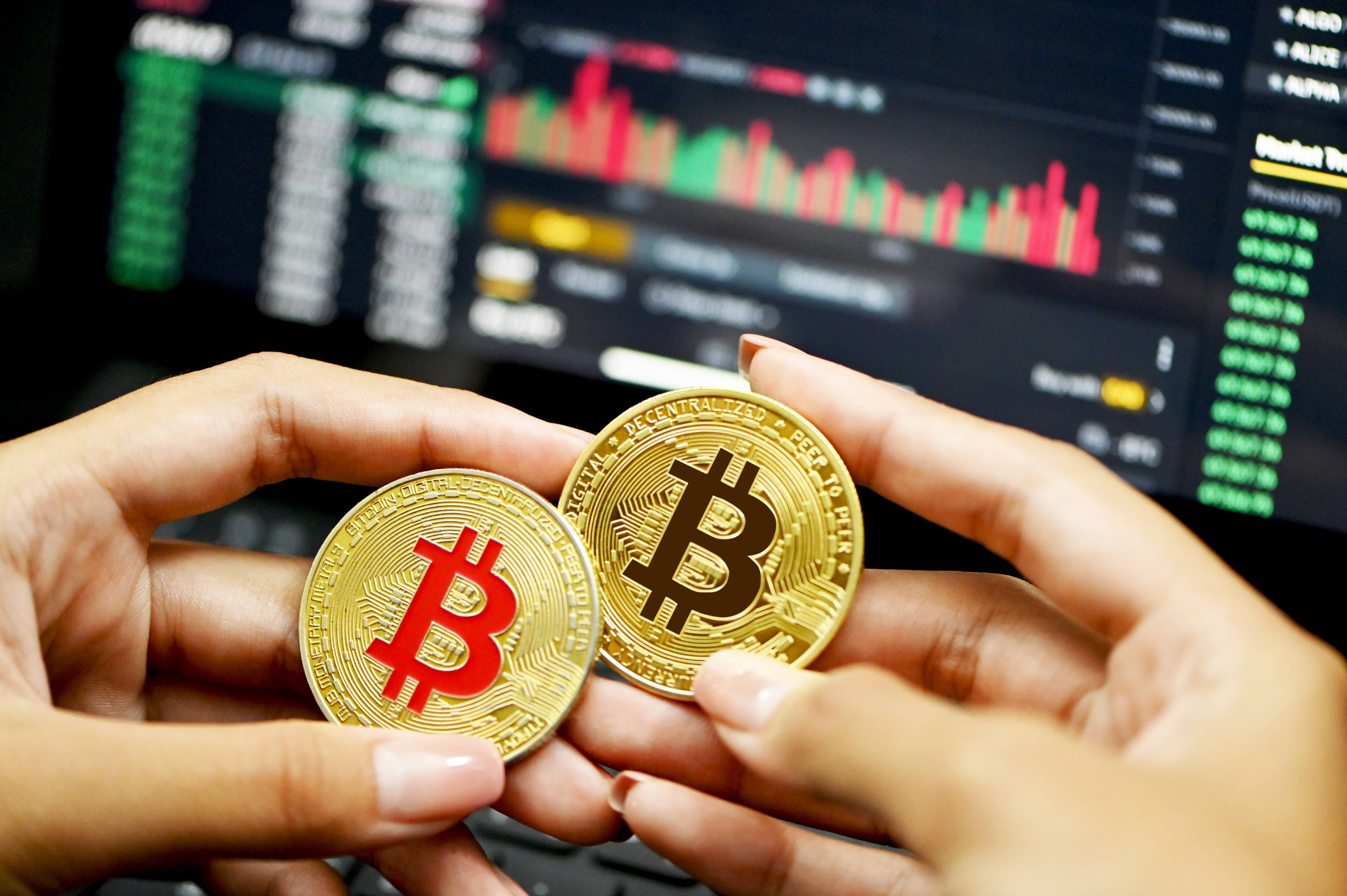 Cryptocurrency 桌布 壁紙 — 雙手在模糊的加密貨幣交易圖表前拿著兩枚金色比特幣。