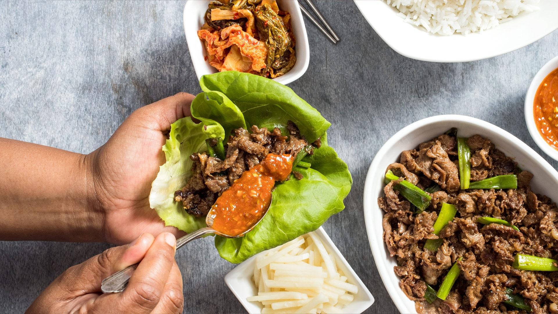 Vegetables 桌布 壁紙 — 雙手在灰色桌子上，用辣醬和各種小菜組裝韓國生菜包。
