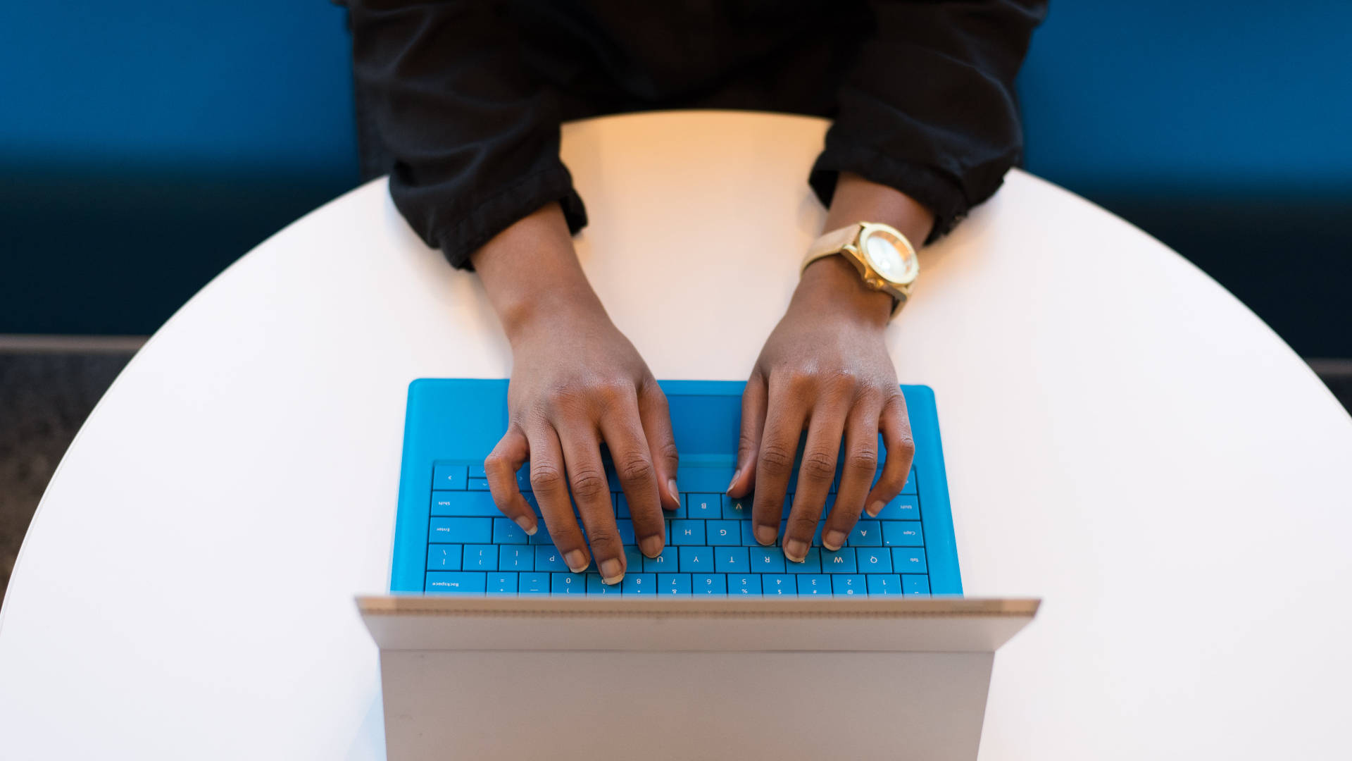 typing 桌布 壁紙 — 雙手在白色圓桌上的藍色筆記型電腦鍵盤上打字的特寫，可見一隻金色手錶。