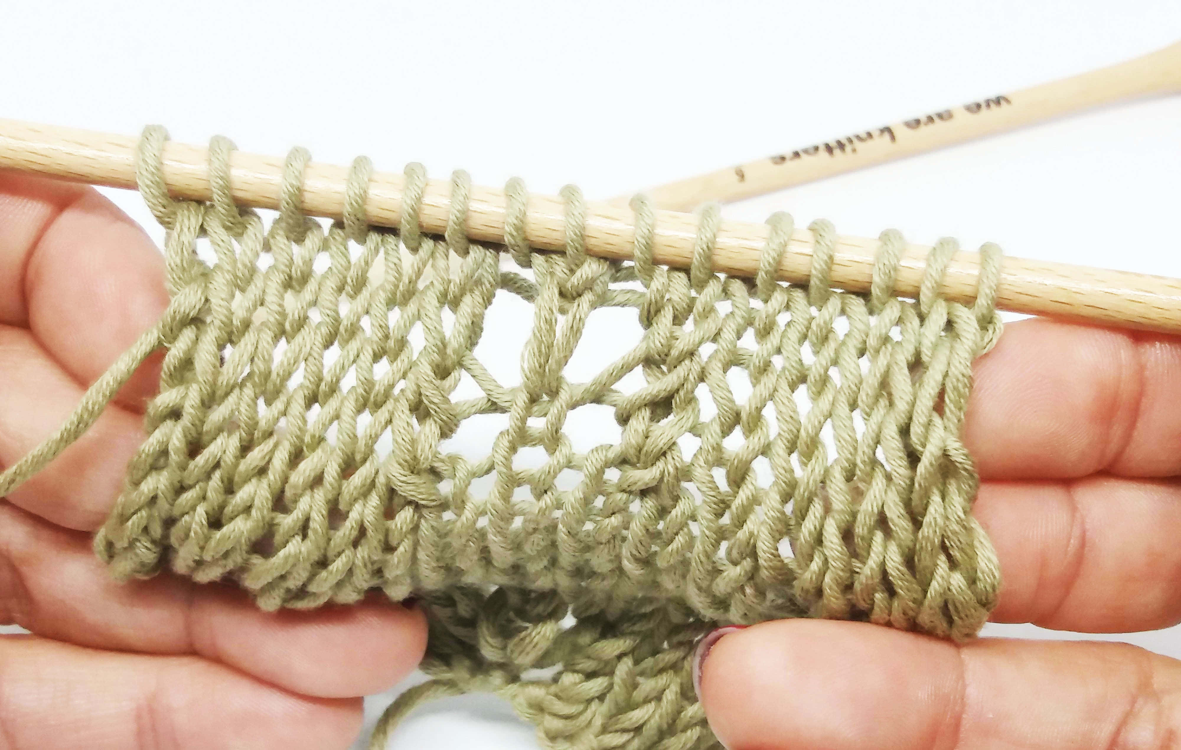 Butterfly Stitch 桌布 壁紙 — 雙手在白色背景前，用木製織針拿著一塊淺綠色蕾絲圖案的編織樣本。