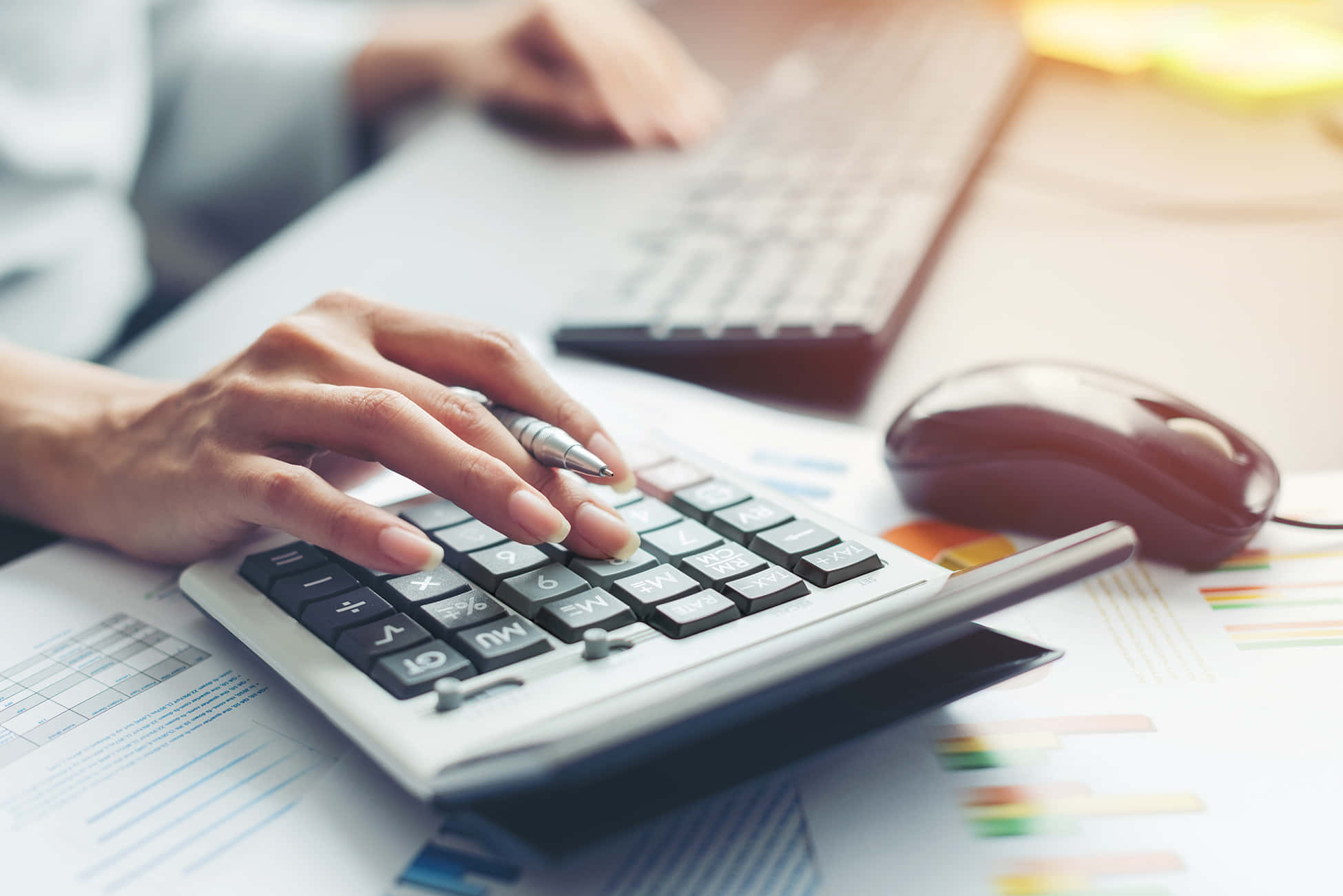 Accounting 桌布 壁紙 — 雙手在辦公桌上使用計算機的特寫，周圍有財務圖表和電腦滑鼠。