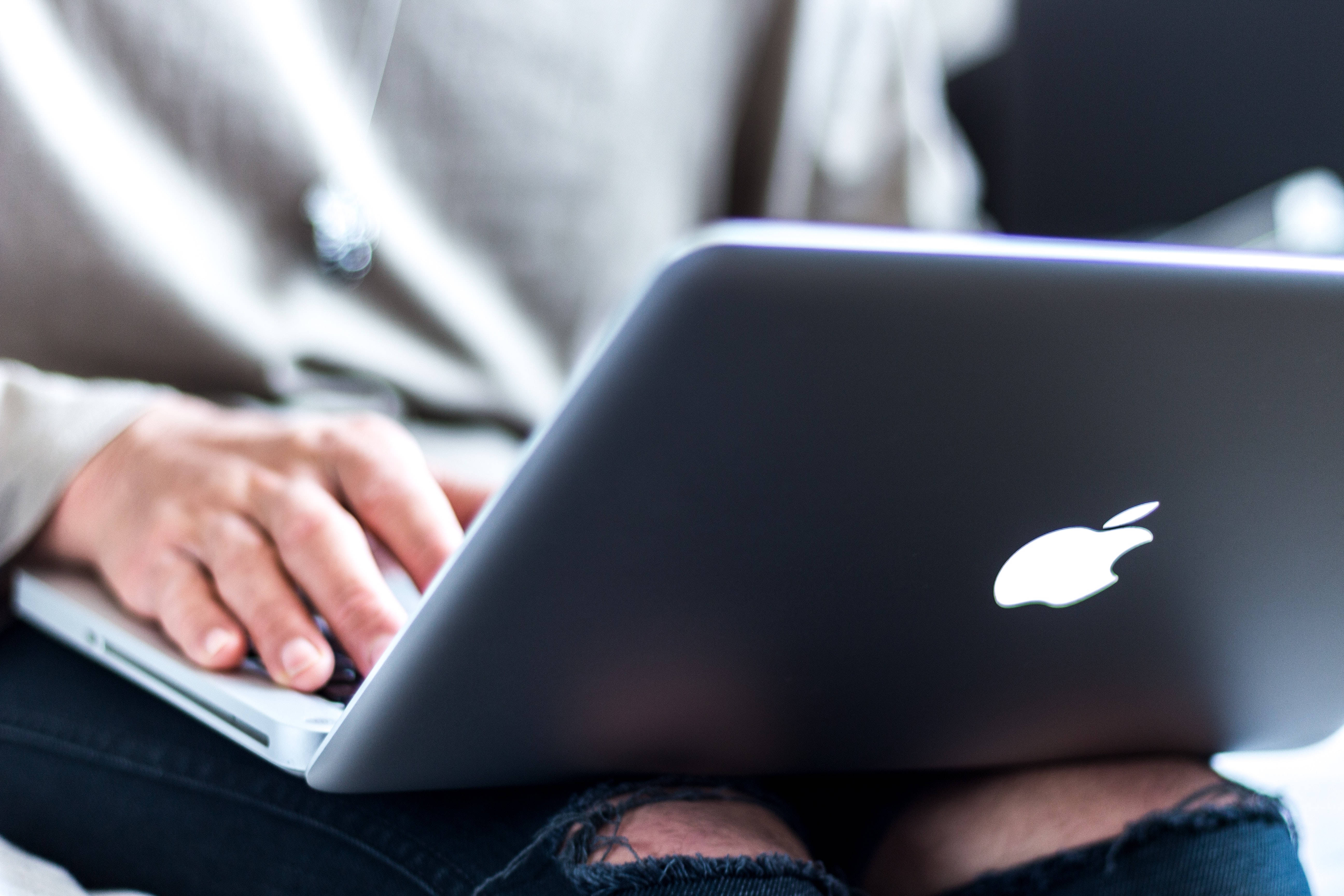 MacBook 動態圖片 桌布 壁紙 — 雙手在銀色筆記型電腦上打字的特寫，電腦放在破洞牛仔褲上，背景柔和模糊。