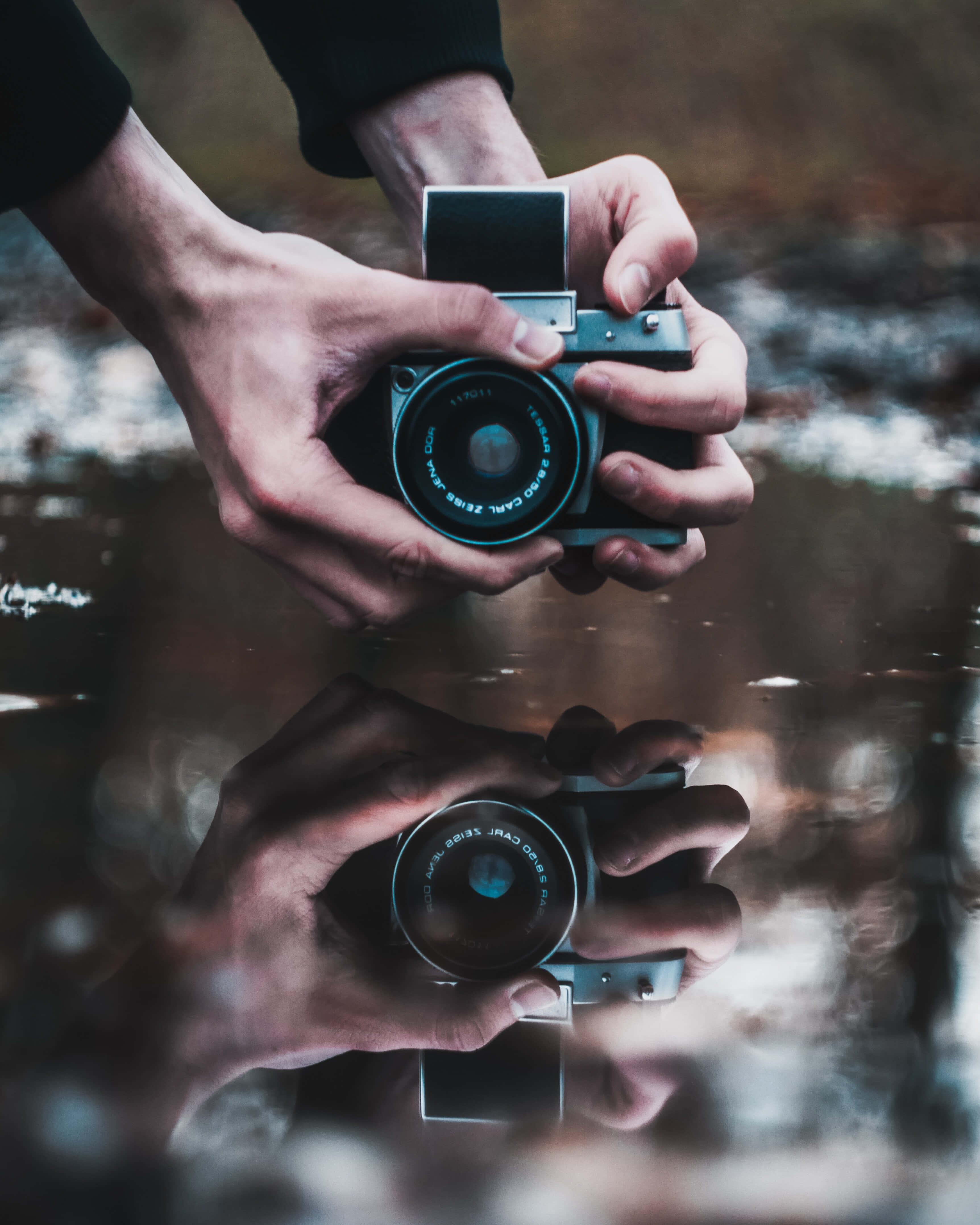reflection 桌布 壁紙 — 雙手將一台復古相機舉在水面上，營造出帶有柔和模糊背景的鏡面倒影。