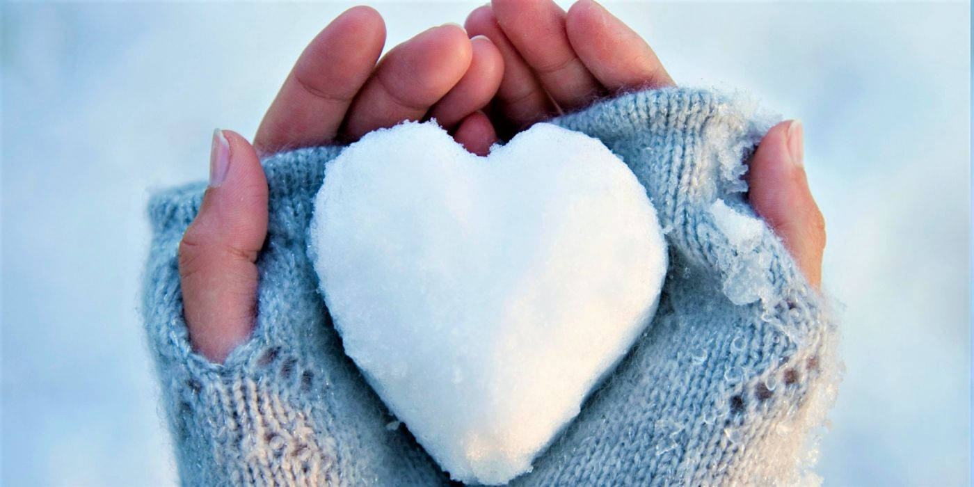White Heart 桌布 壁紙 — 雙手戴著柔軟的藍色針織手套，在雪景背景下輕輕捧著一個純白的雪心。