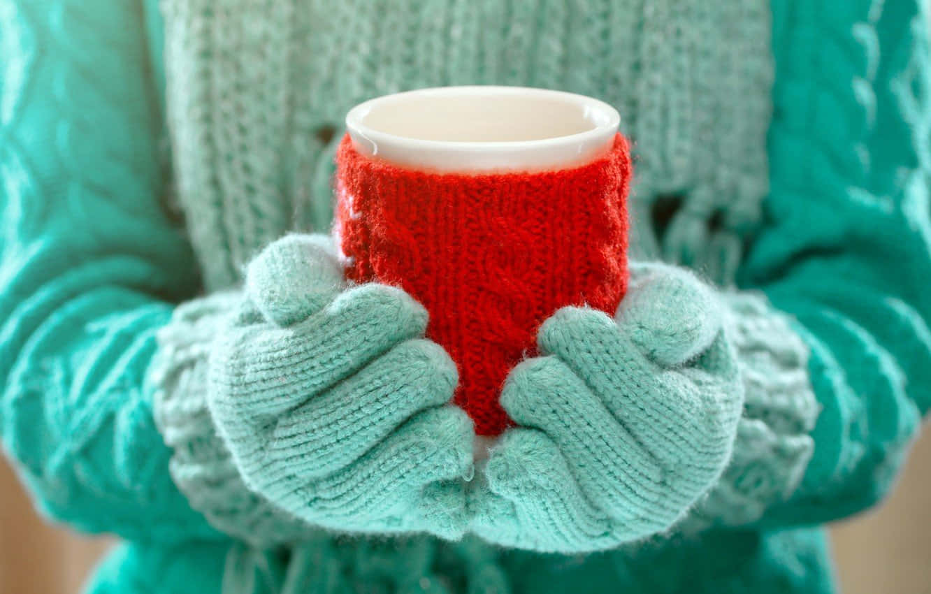 Mittens 桌布 壁紙 — 雙手戴著青綠色針織手套，捧著一個紅色針織馬克杯，背景是舒適的青綠色針織毛衣。