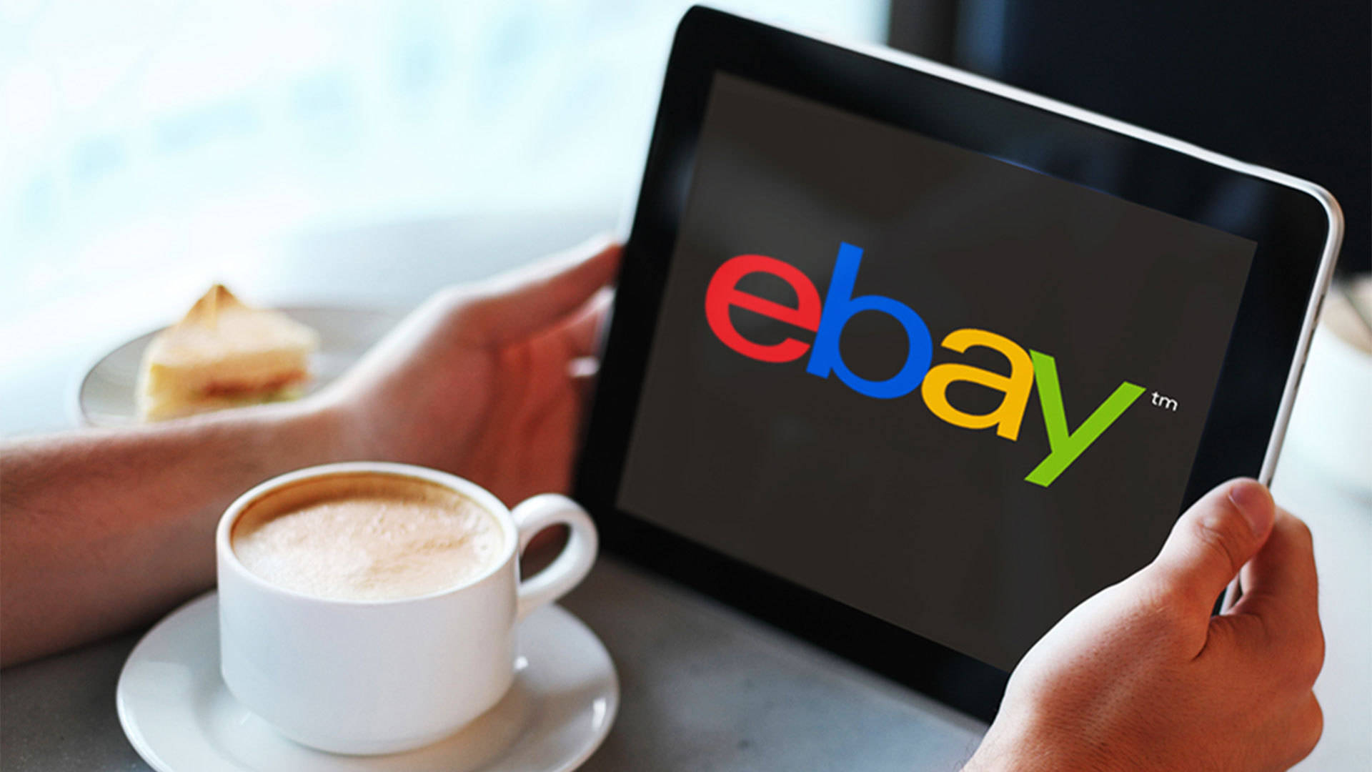 eBay 桌布 壁紙 — 雙手拿著一台顯示eBay標誌的平板電腦，旁邊放著一杯咖啡和一片蛋糕在桌上。
