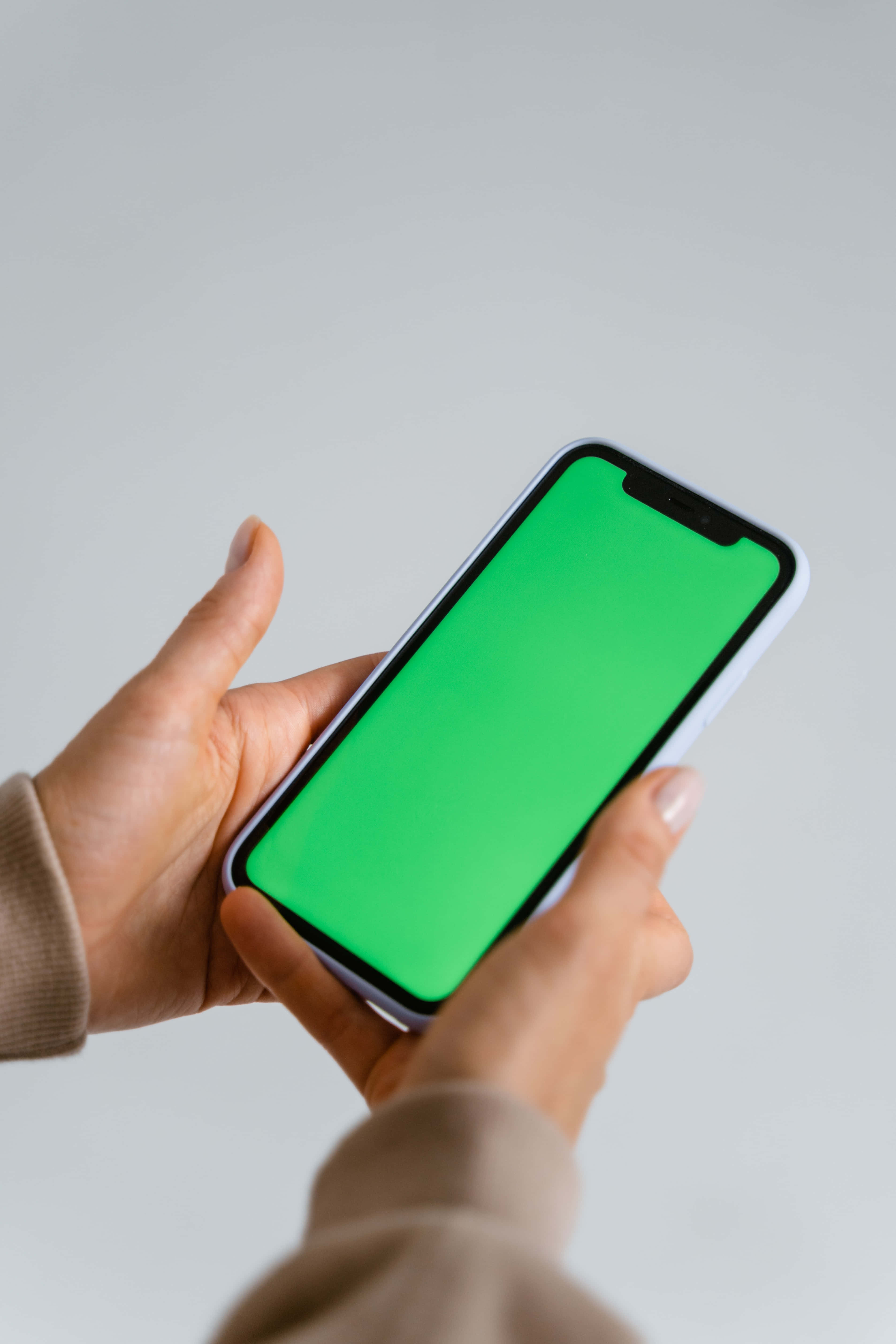 iPhone 桌布 壁紙 — 雙手拿著一部螢幕亮綠色的智慧型手機，背景是純淺灰色。