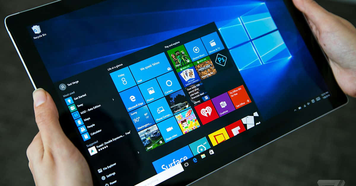 Windows Aesthetic 桌布 壁紙 — 雙手拿著平板電腦，顯示Windows 10開始功能表，帶有彩色應用程式磚和藍色背景。