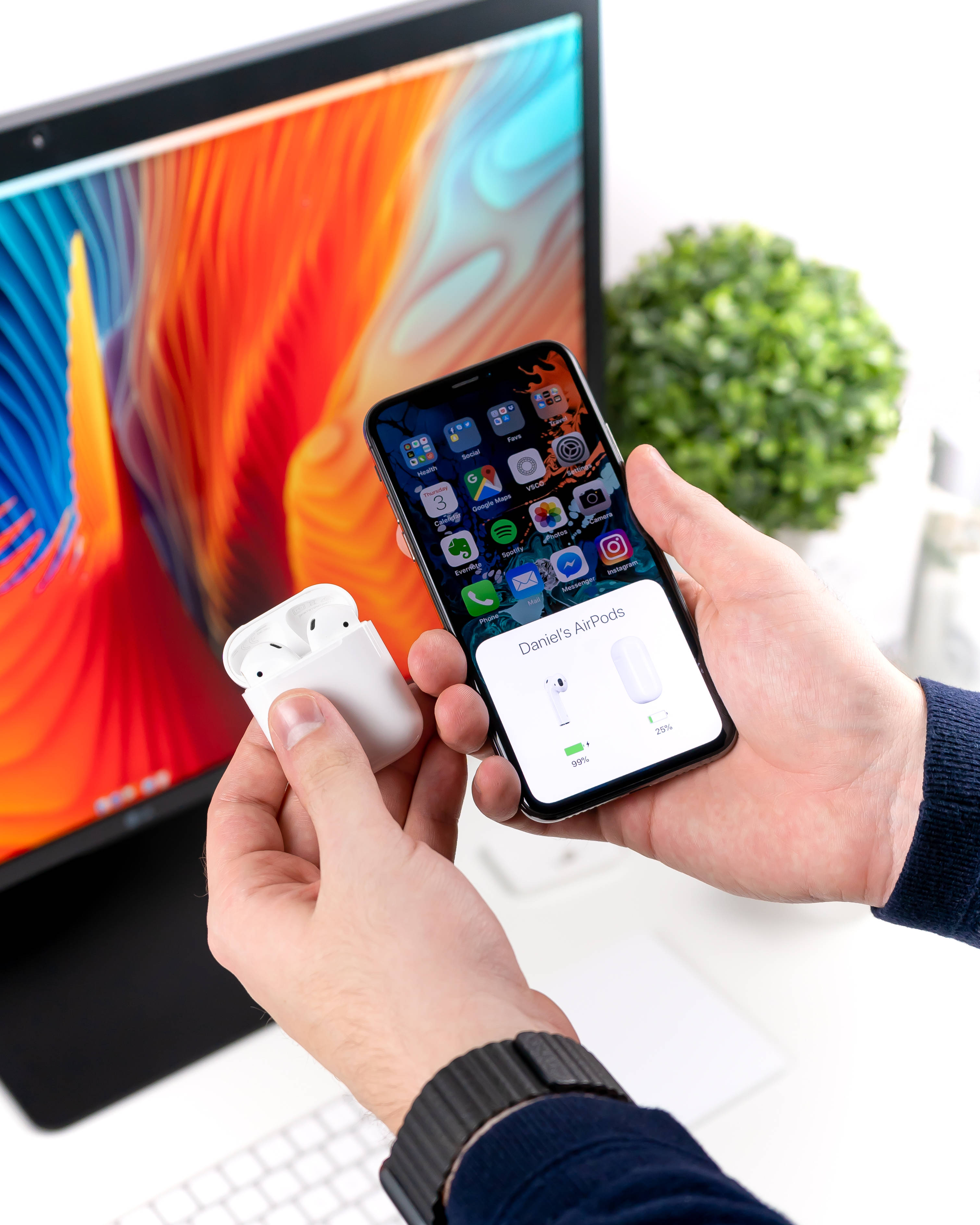 Airpods 桌布 壁紙 — 雙手拿著白色AirPods保護殼和手機，顯示藍牙配對畫面，背景有彩色顯示器。