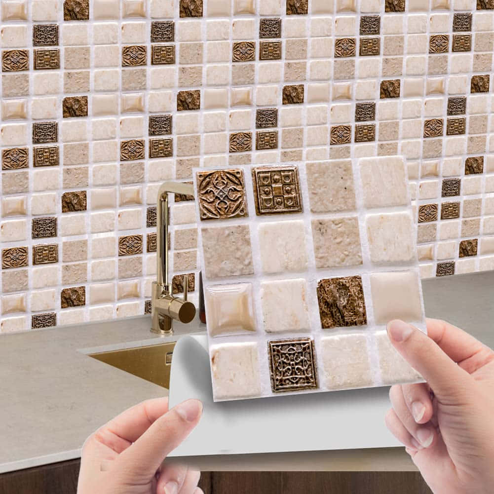 Tiles 桌布 壁紙 — 雙手拿著米色和金色紋理馬賽克瓷磚樣本，對應現代廚房水槽上方的匹配防濺板。