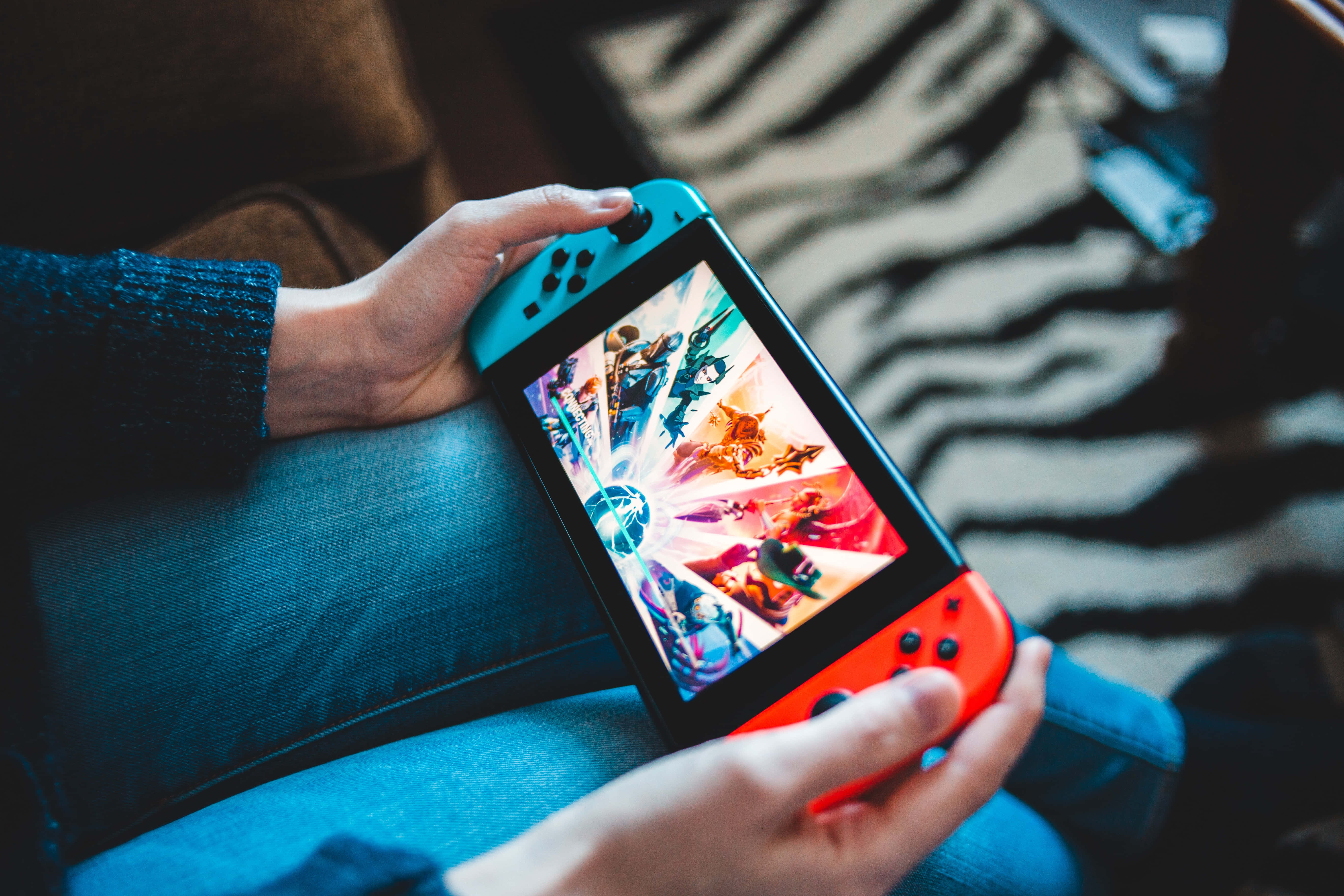 Gaming Consoles 桌布 壁紙 — 雙手拿著紅藍色的Nintendo Switch，在斑馬紋沙發上玩充滿活力的動作遊戲。